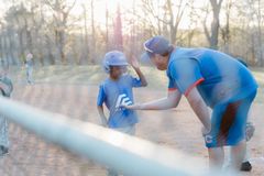 Coach in blue helps a child in a blue helmet at a baseball field during practice