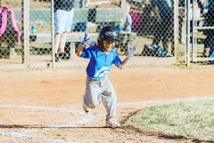 Young baseball player in blue uniform running toward home plate on a dirt field