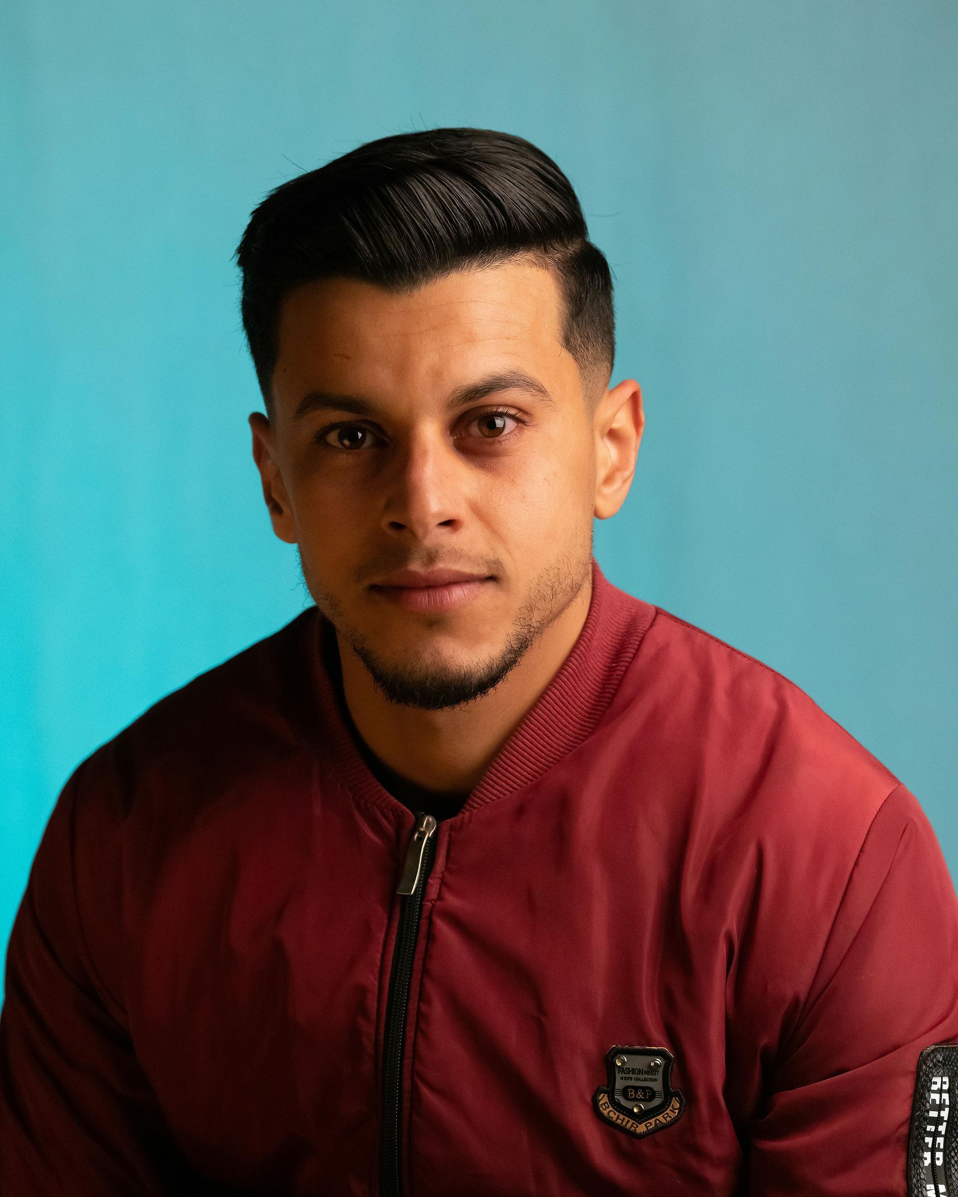 Portrait of a man in a maroon jacket against a teal background.