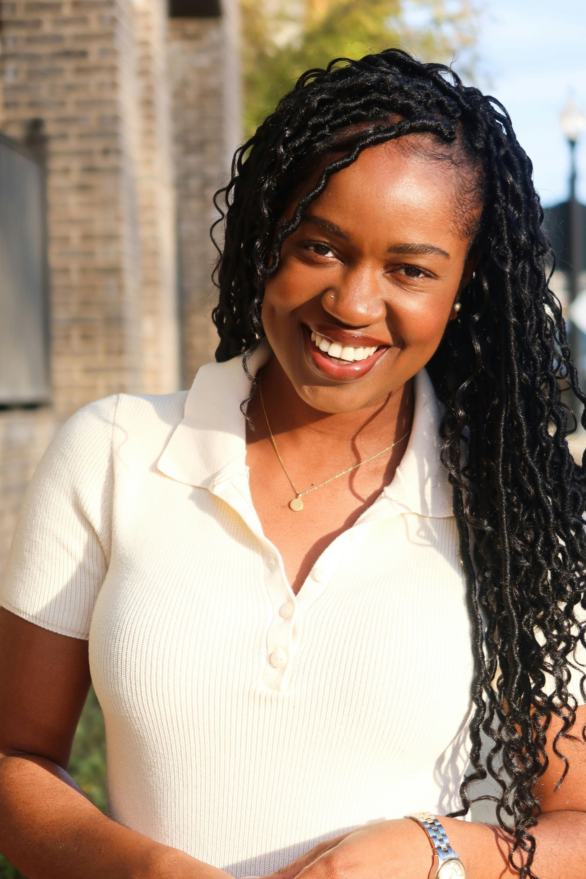 Smiling person in a white top standing outdoors in sunlight