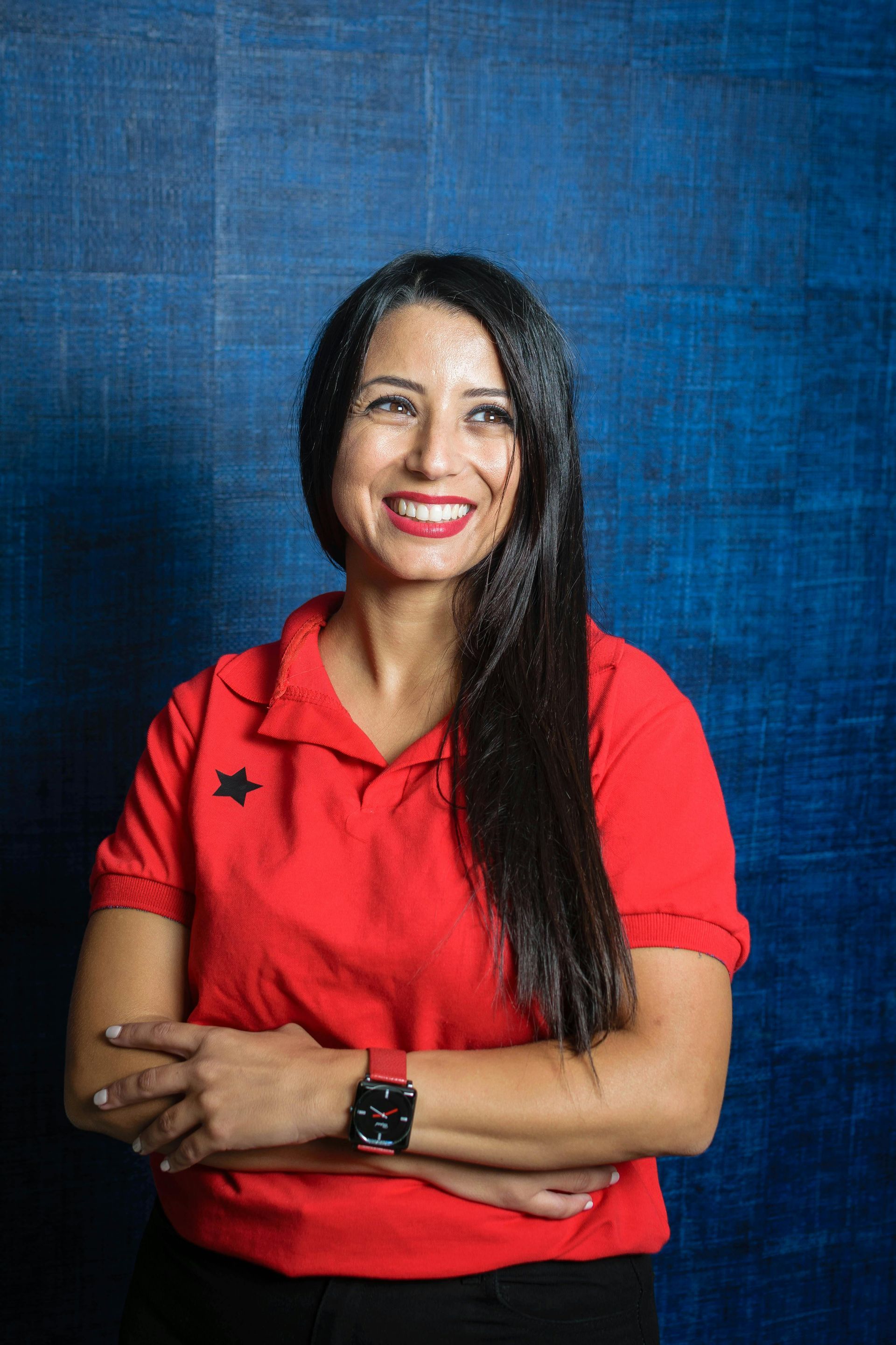 Smiling woman in a red shirt with crossed arms against a blue background