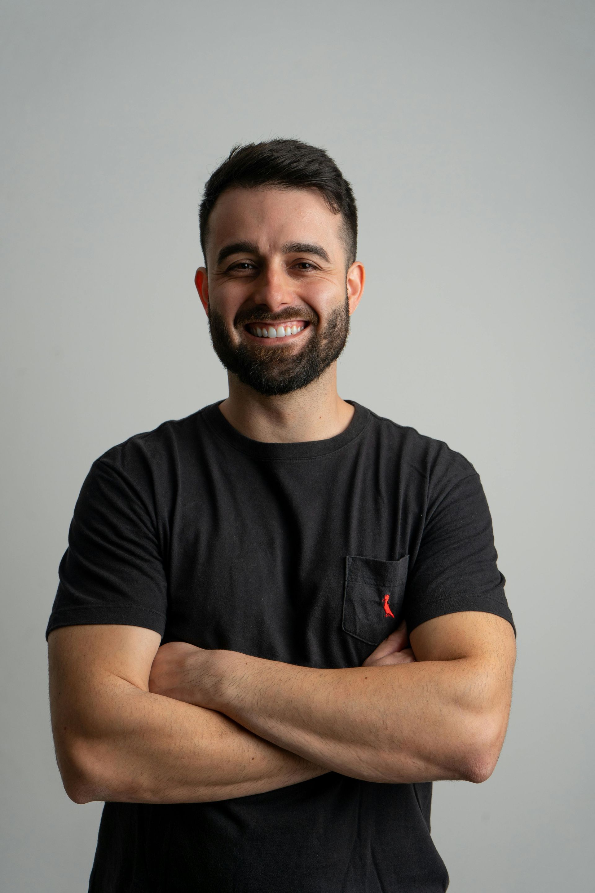 Smiling person in a black T-shirt with arms crossed against a plain gray background
