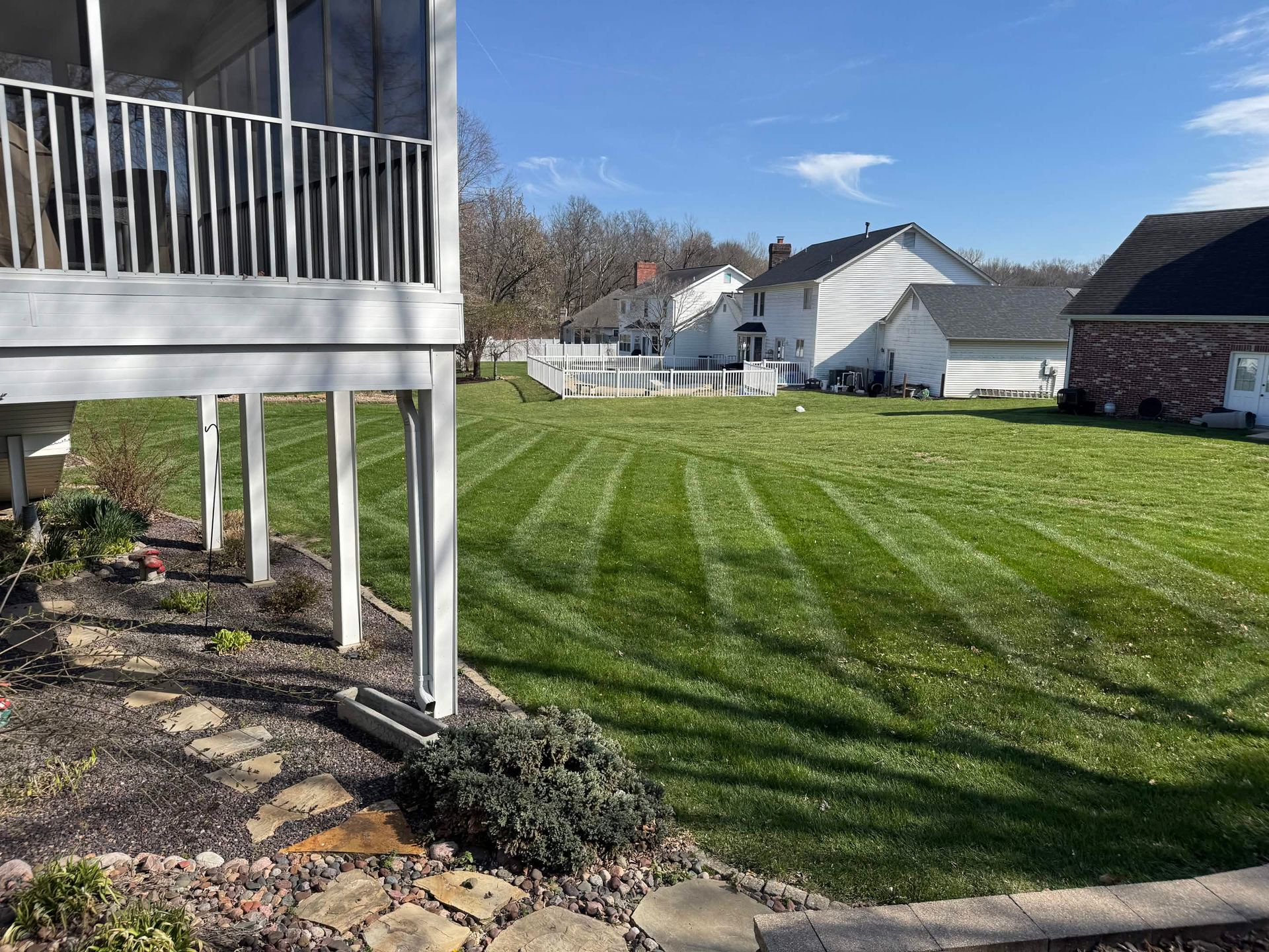 Backyard lawn with a striped green pattern beside a raised deck and neighboring houses.