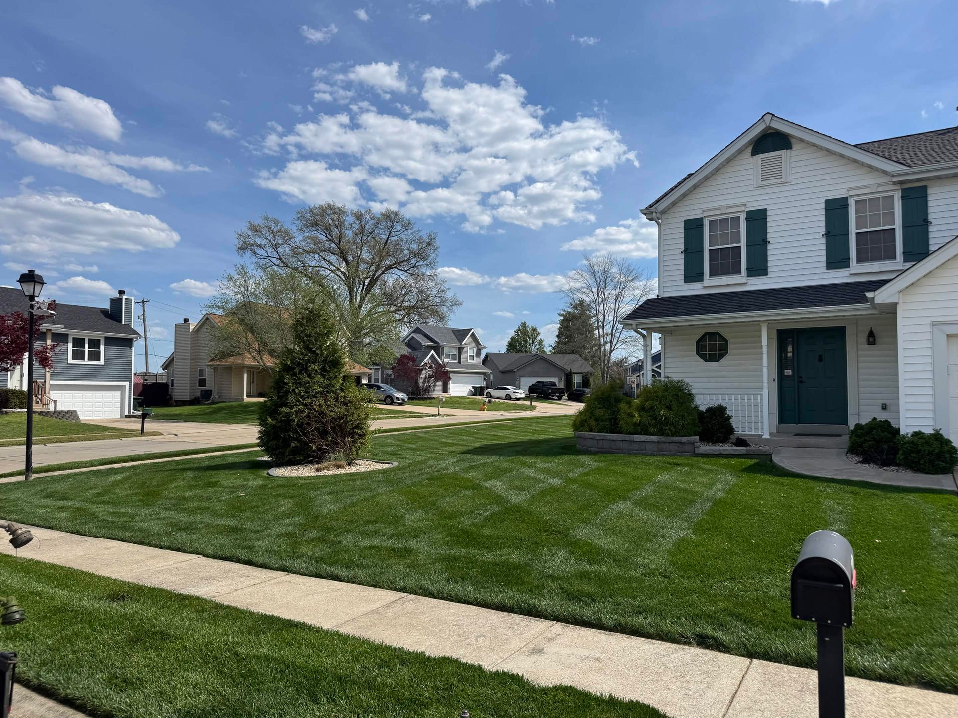 Suburban house with a green lawn, sidewalk, mailbox, and partly cloudy blue sky