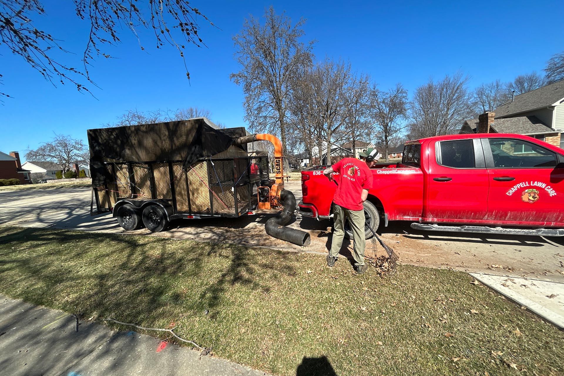 Red pickup truck and workers beside a trailer in a residential yard on a sunny day