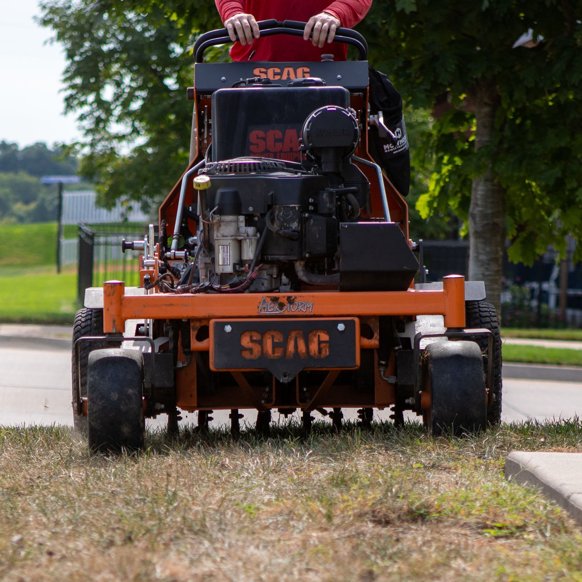 Red zero-turn lawn mower cutting grass along a curb in a park-like area