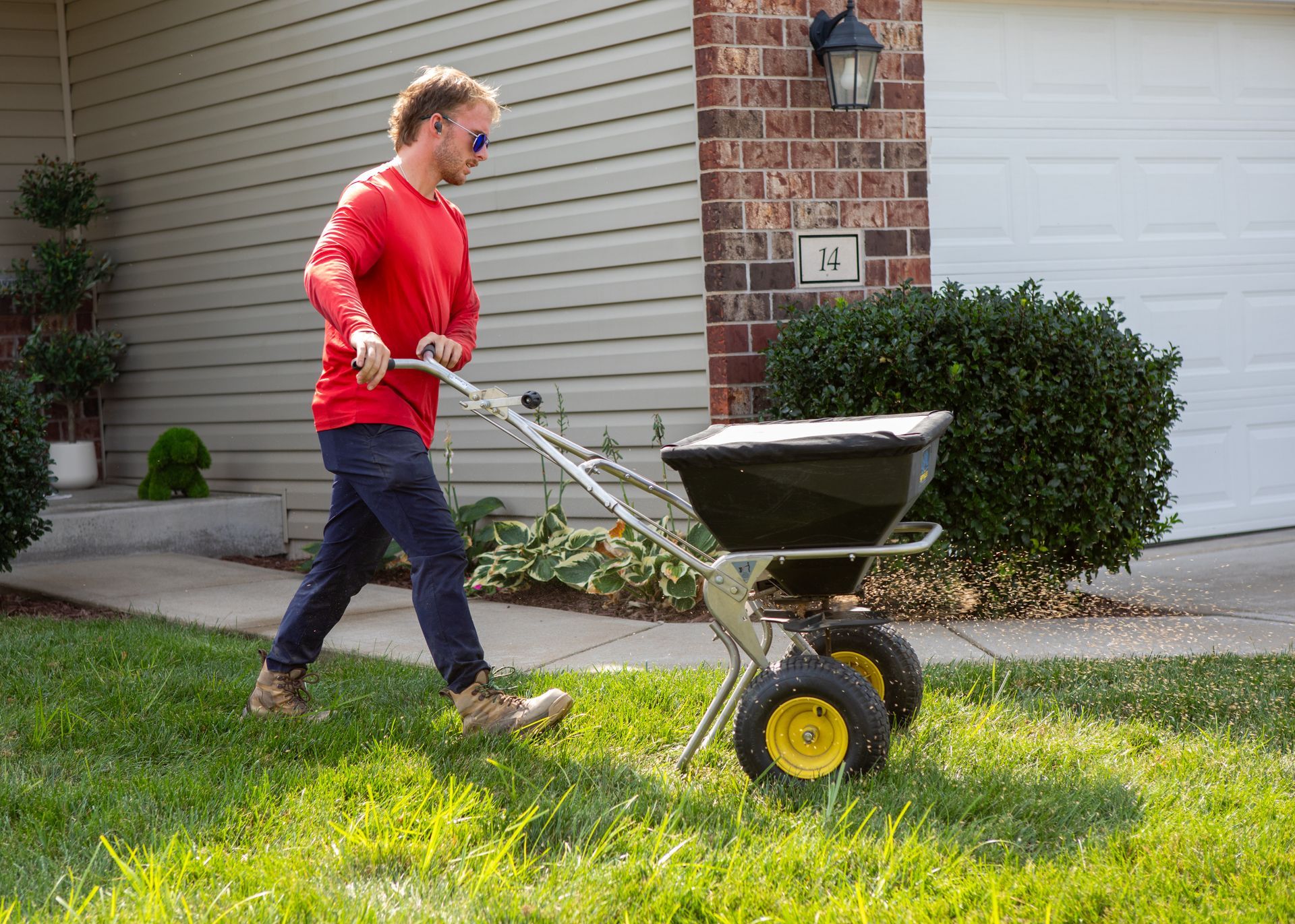 Person in a red sweater pushing a wheelbarrow across a grassy lawn beside a house.