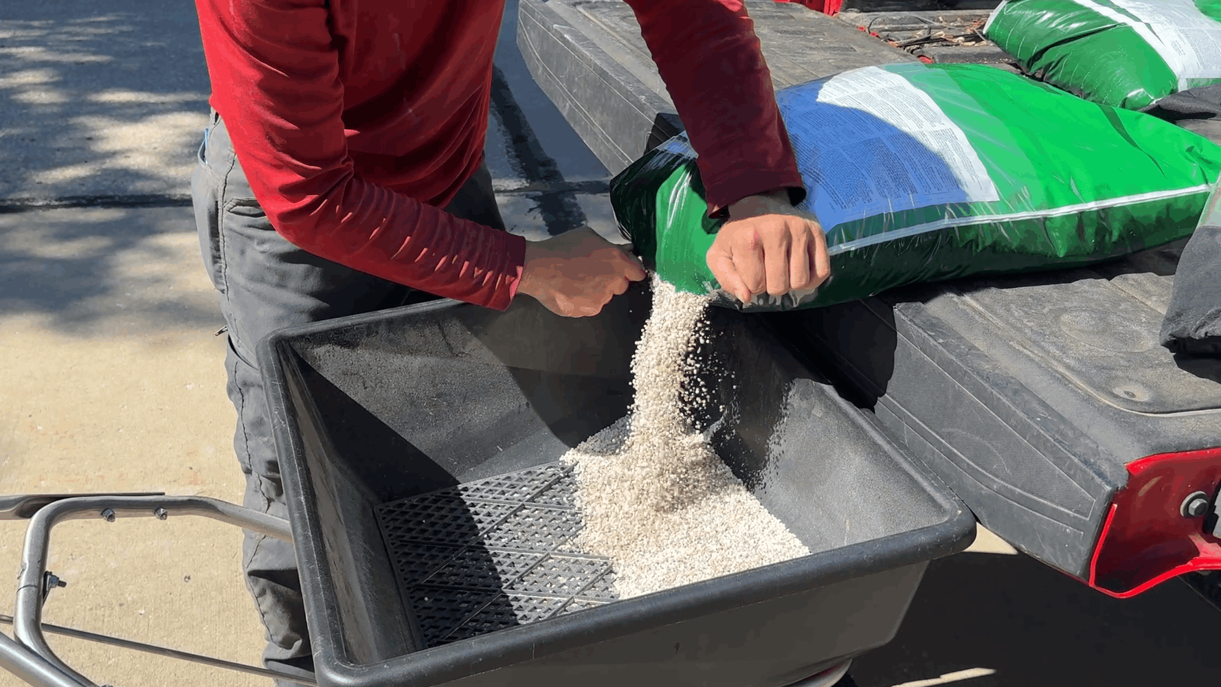 Pouring white pellets from a bag into a wheelbarrow on a driveway