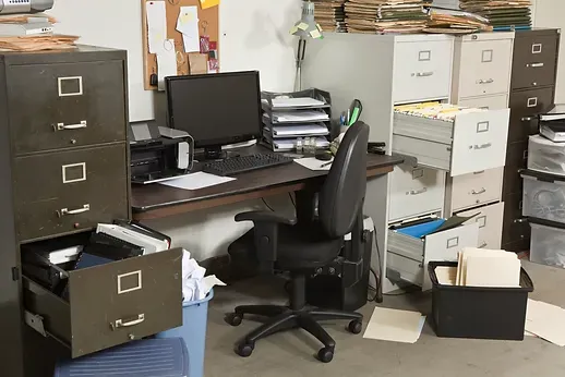 A cluttered office with a desk , chair , filing cabinets and a computer.