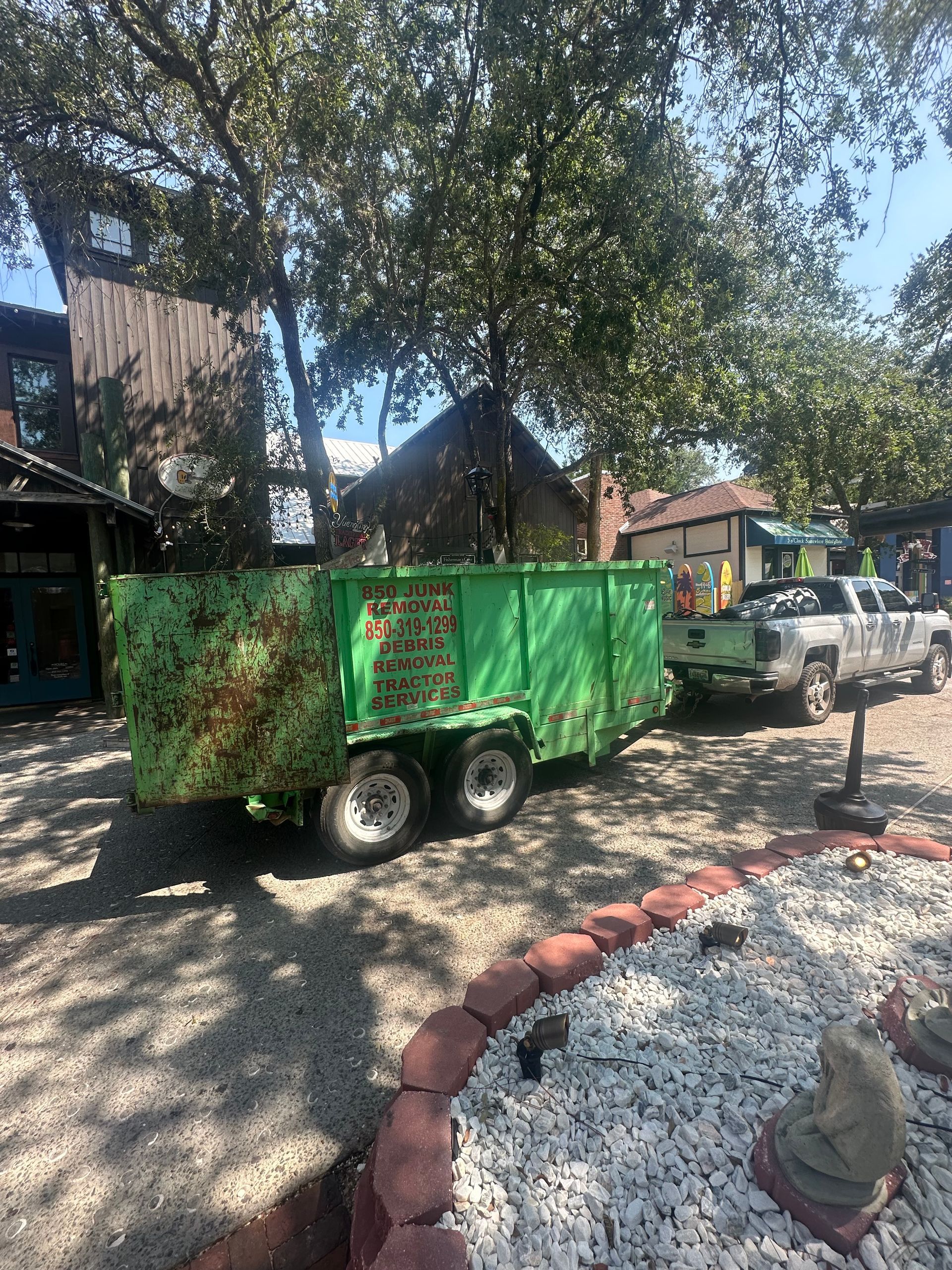 A green dumpster trailer is parked in a driveway next to a truck.