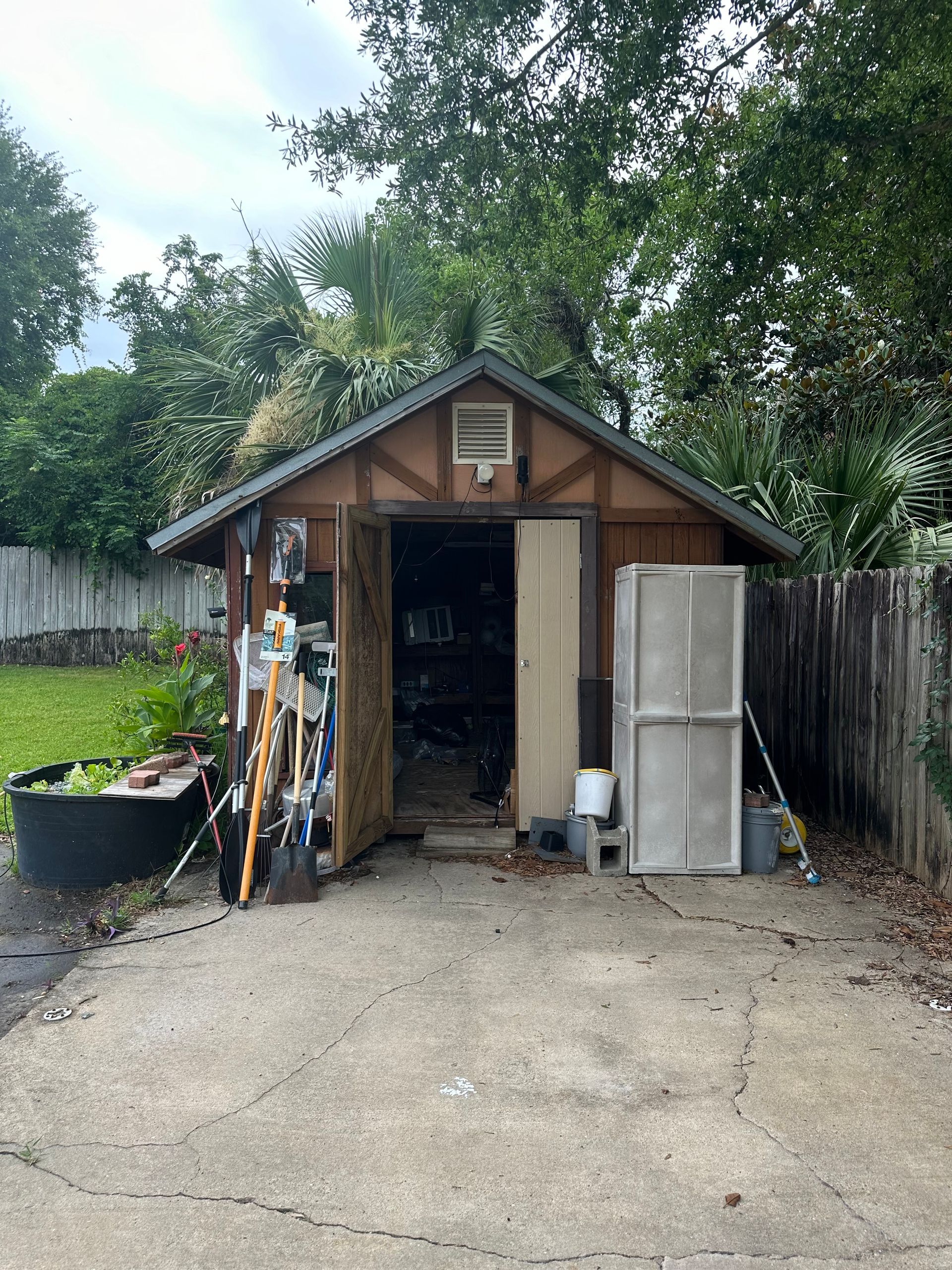 A wooden shed with a roof is sitting in the middle of a driveway.