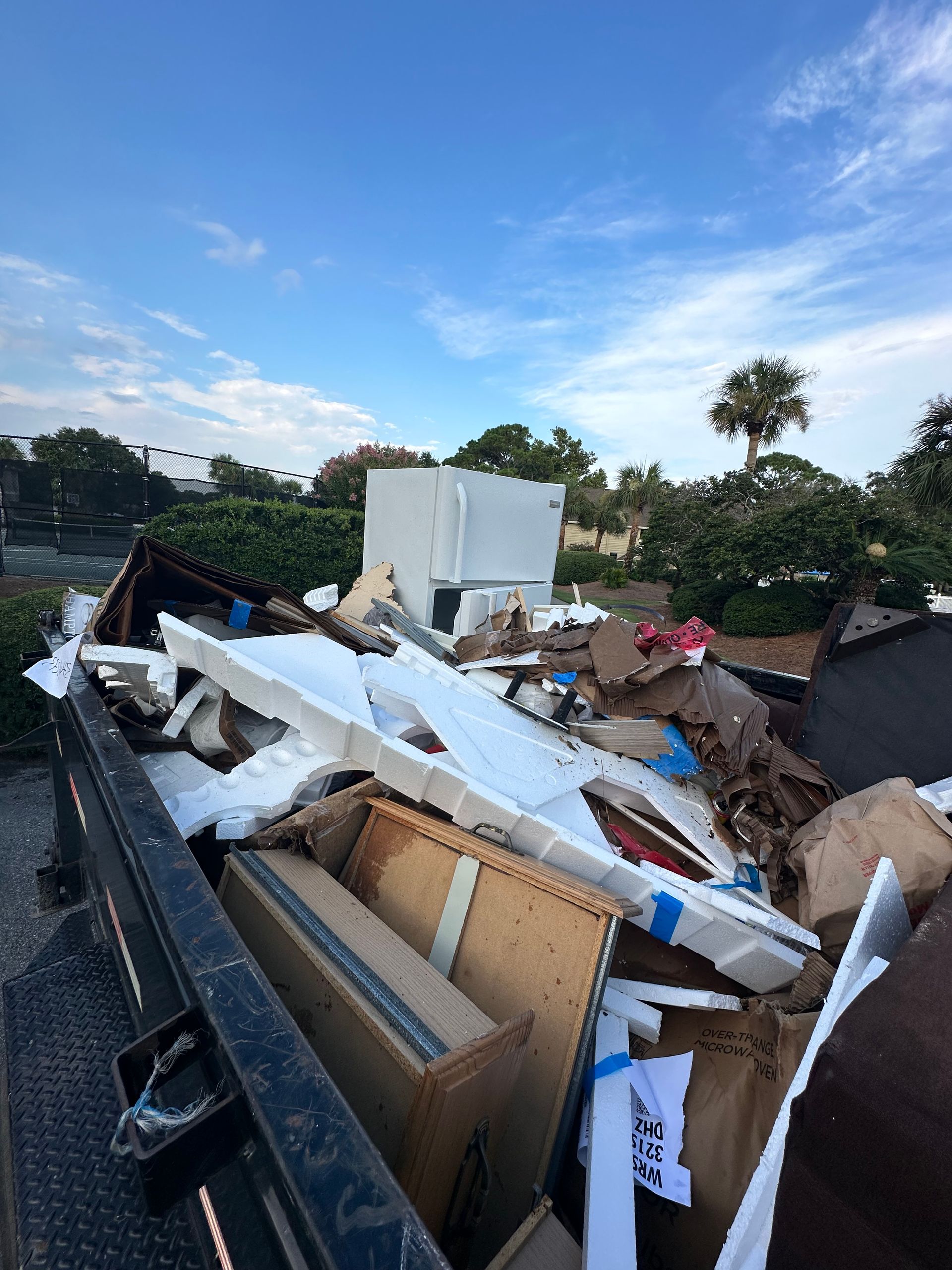 Trailer loaded with old furniture and debris under palm trees, condo cleanouts in Miramar Beach and Sandestin, FL