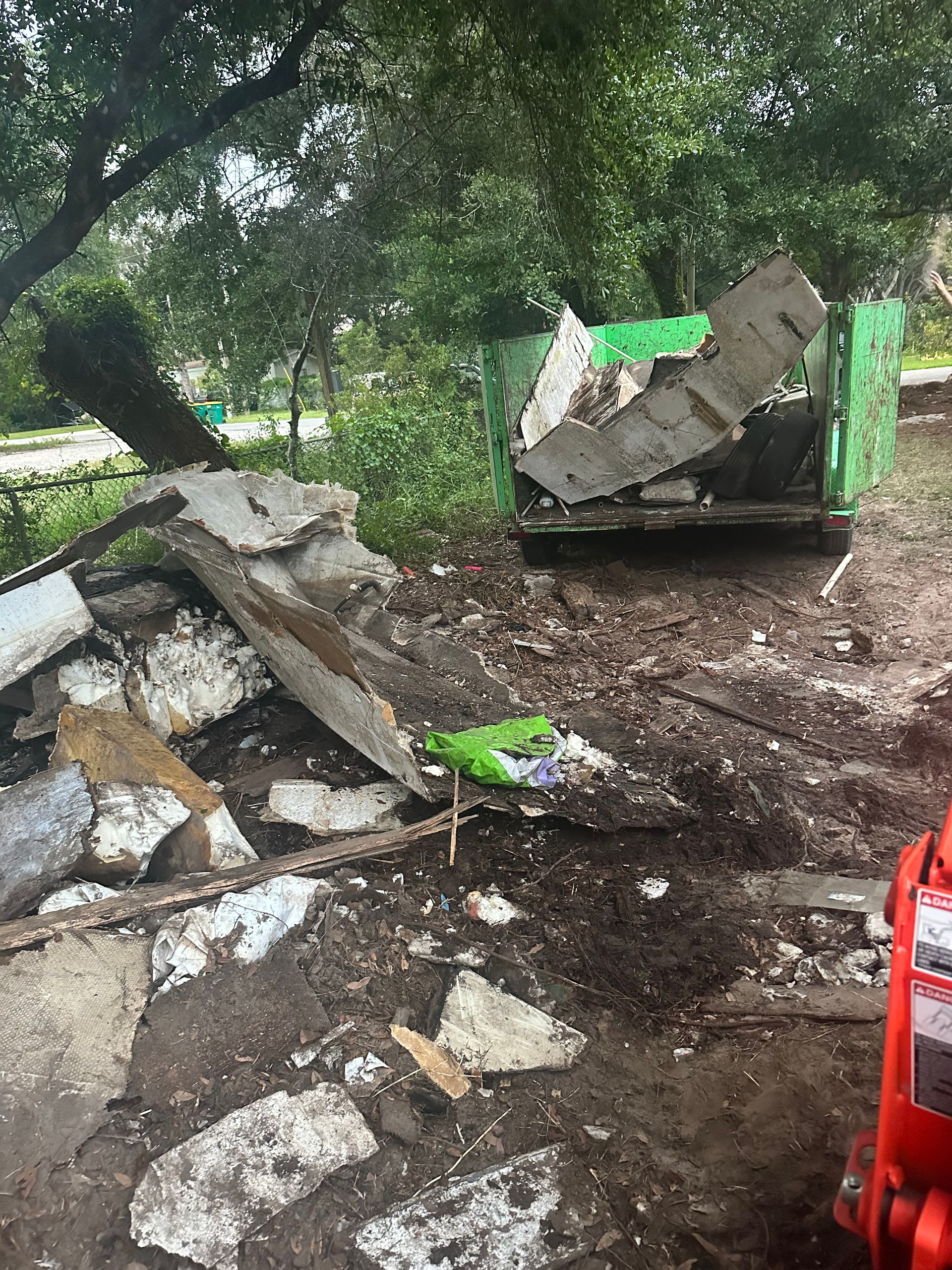 A dumpster is sitting in the dirt next to a pile of rubble.