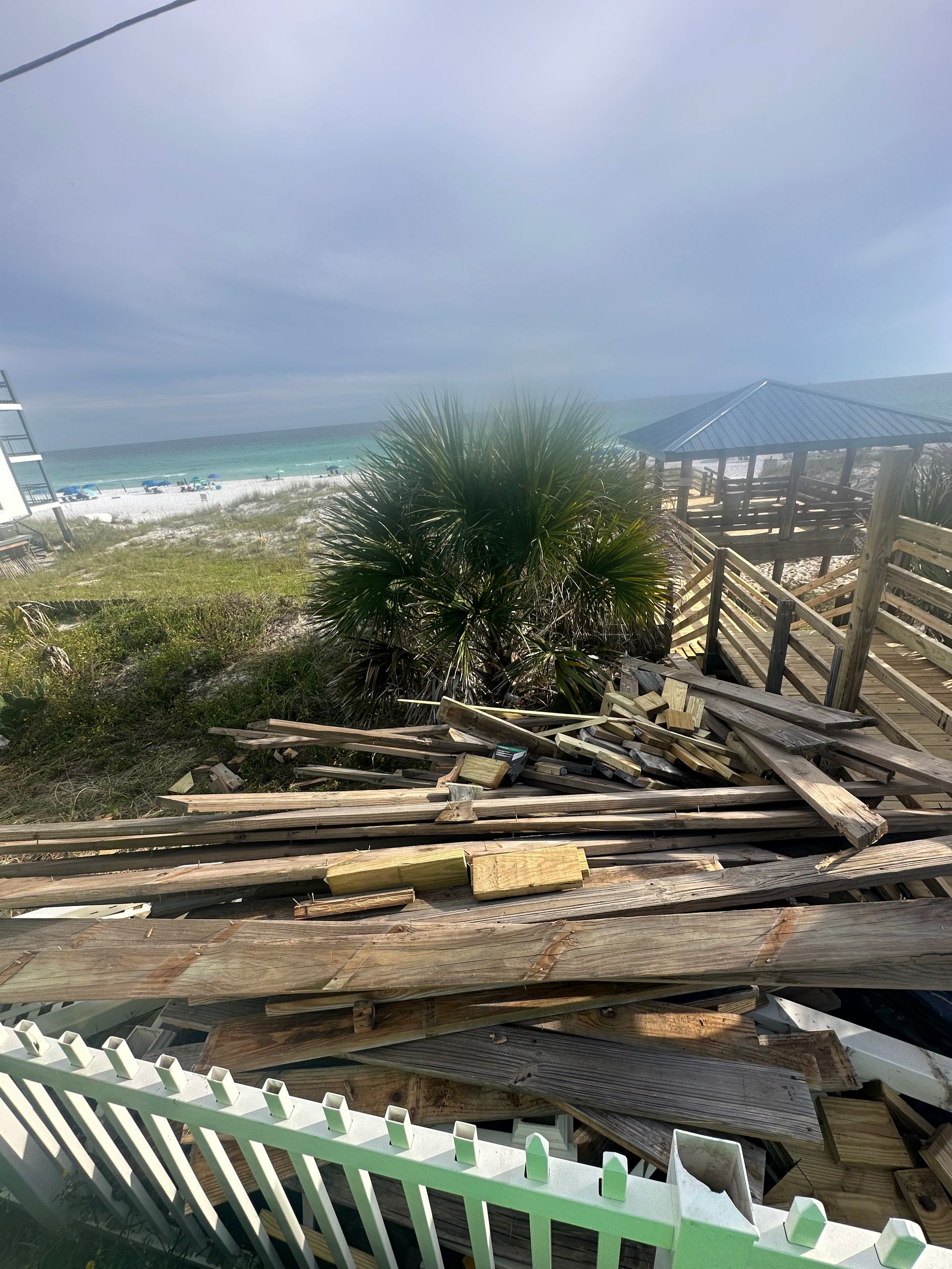 A pile of wood is sitting in front of a fence with a view of the ocean.