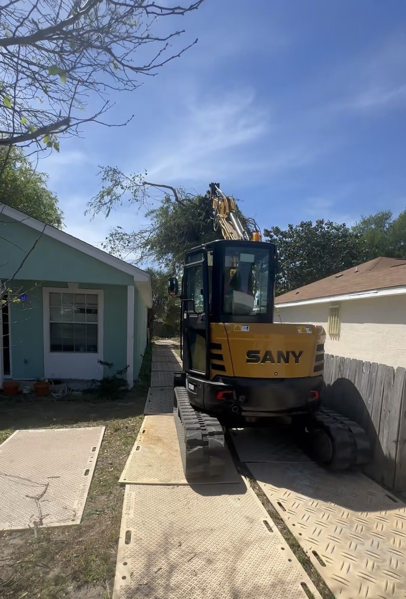 Mini excavator working between two houses on ground mats that protect the lawn