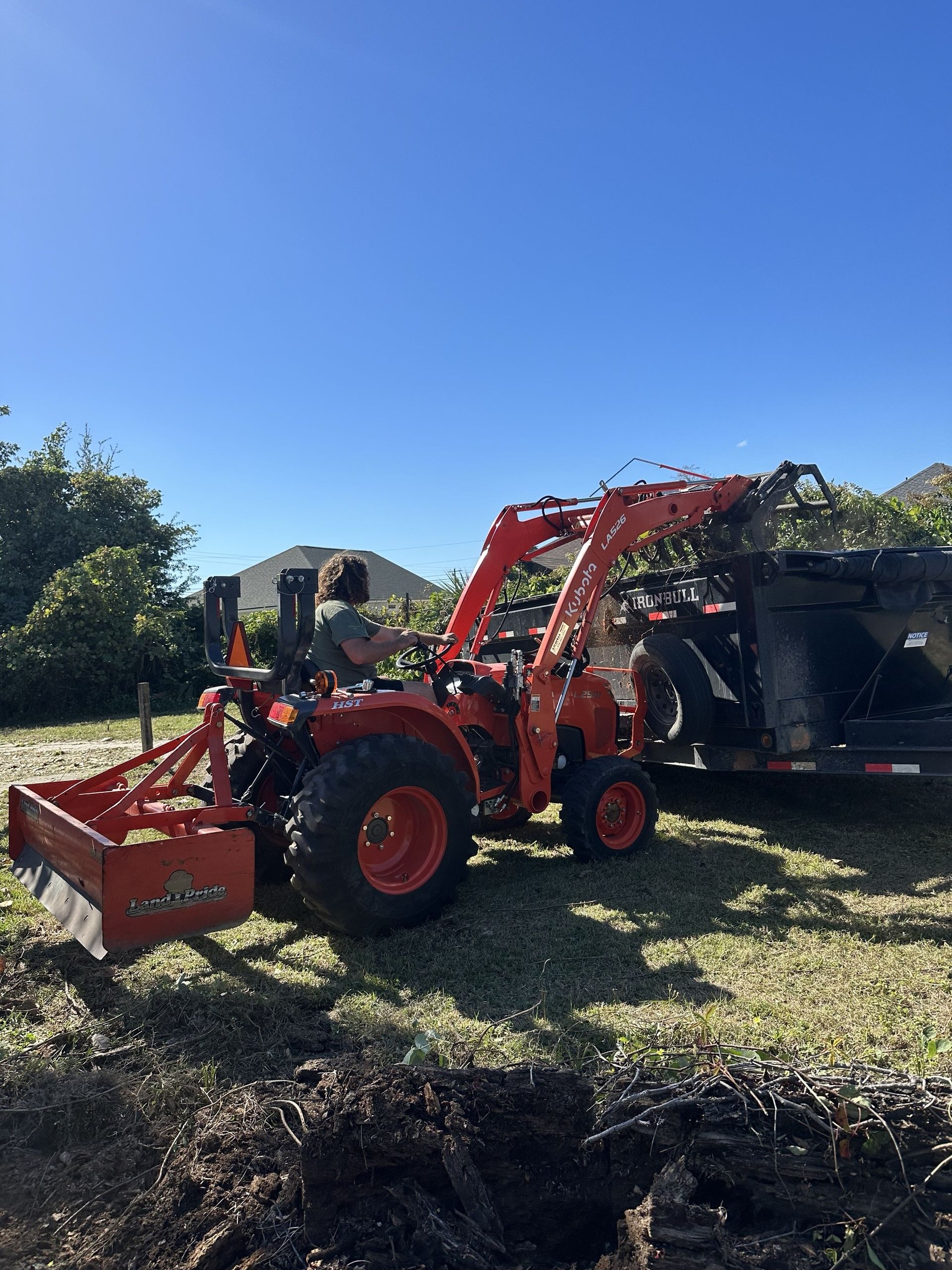 850 Junk Removal's Kubota tractor dumping a grapple load of brush and debris into our dump trailer