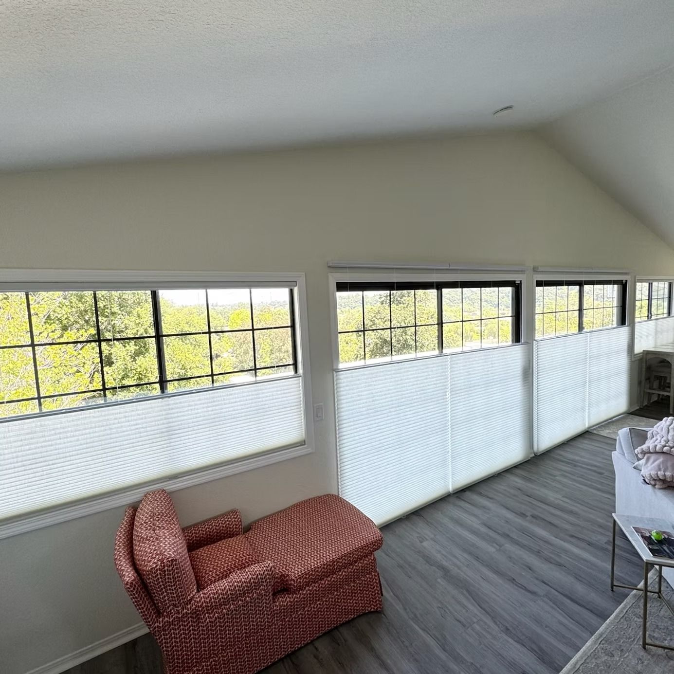 Bright loft-style living area with large windows, white walls, gray floor, and a red patterned chaise lounge.