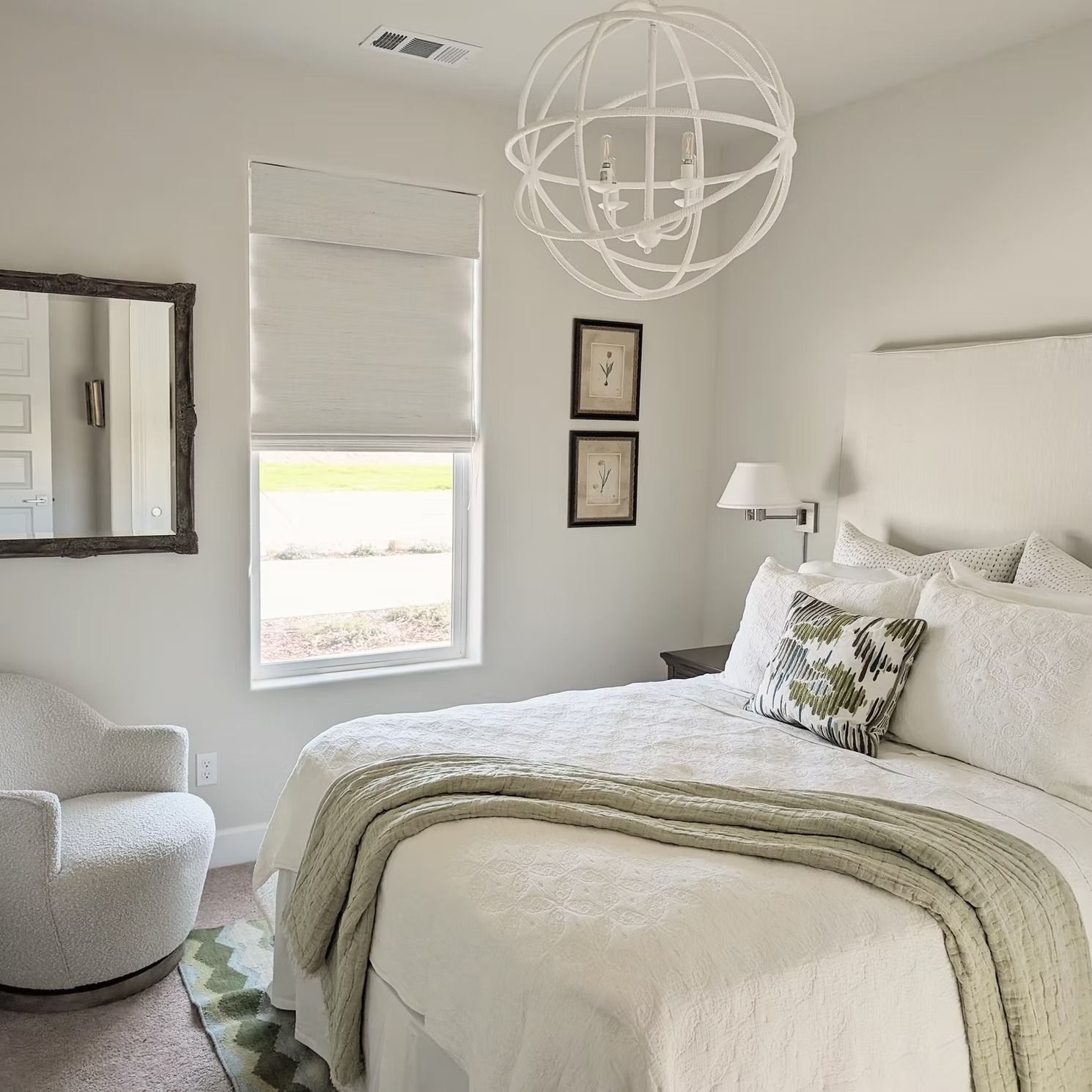 Bright white bedroom with a bed, chair, mirror, window, and globe pendant light