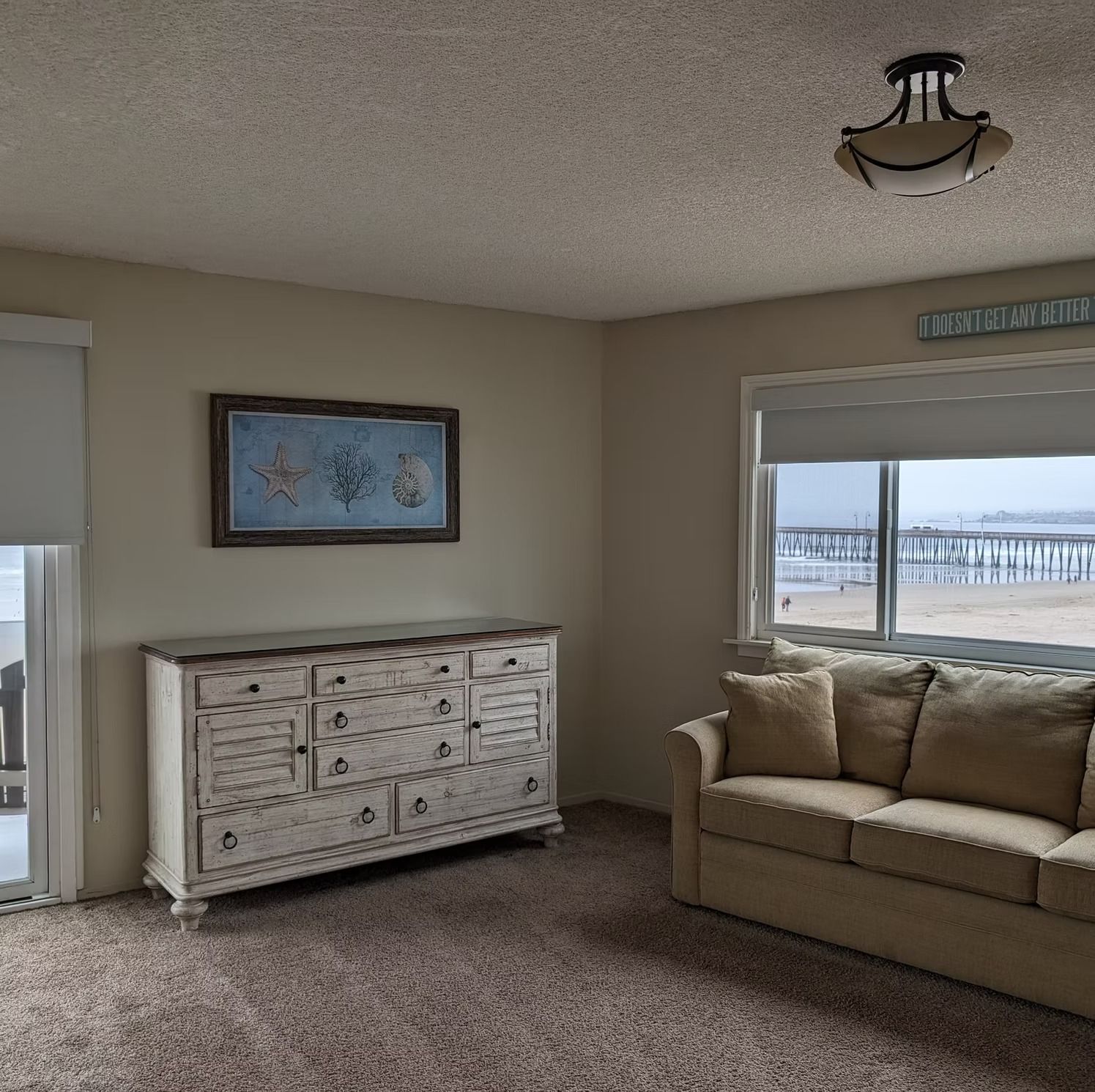 Cozy living room with tan sofa, white dresser, framed art, and windows showing a snowy outdoor view