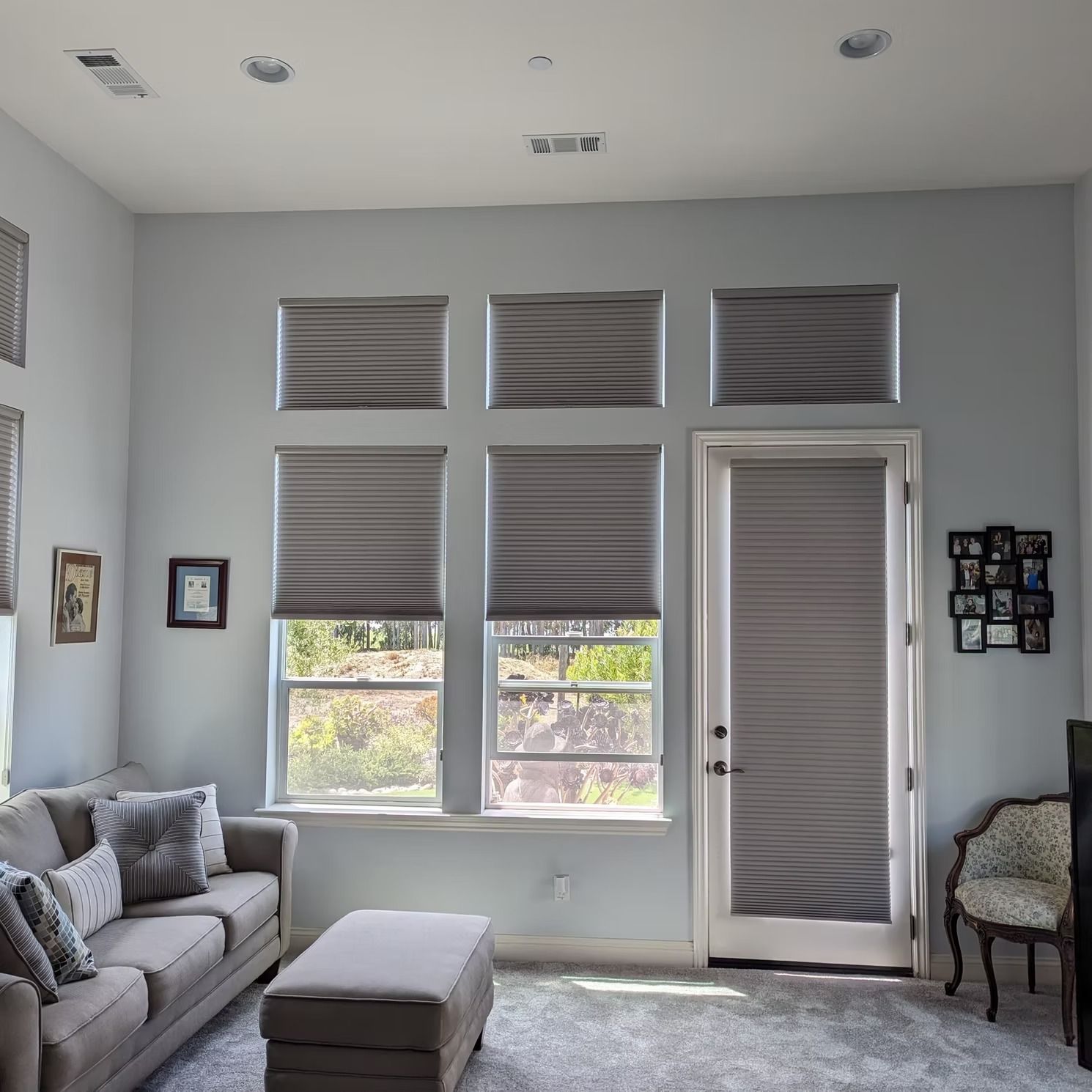 Bright living room with gray sofa, ottoman, large windows, and a glass-paneled door.