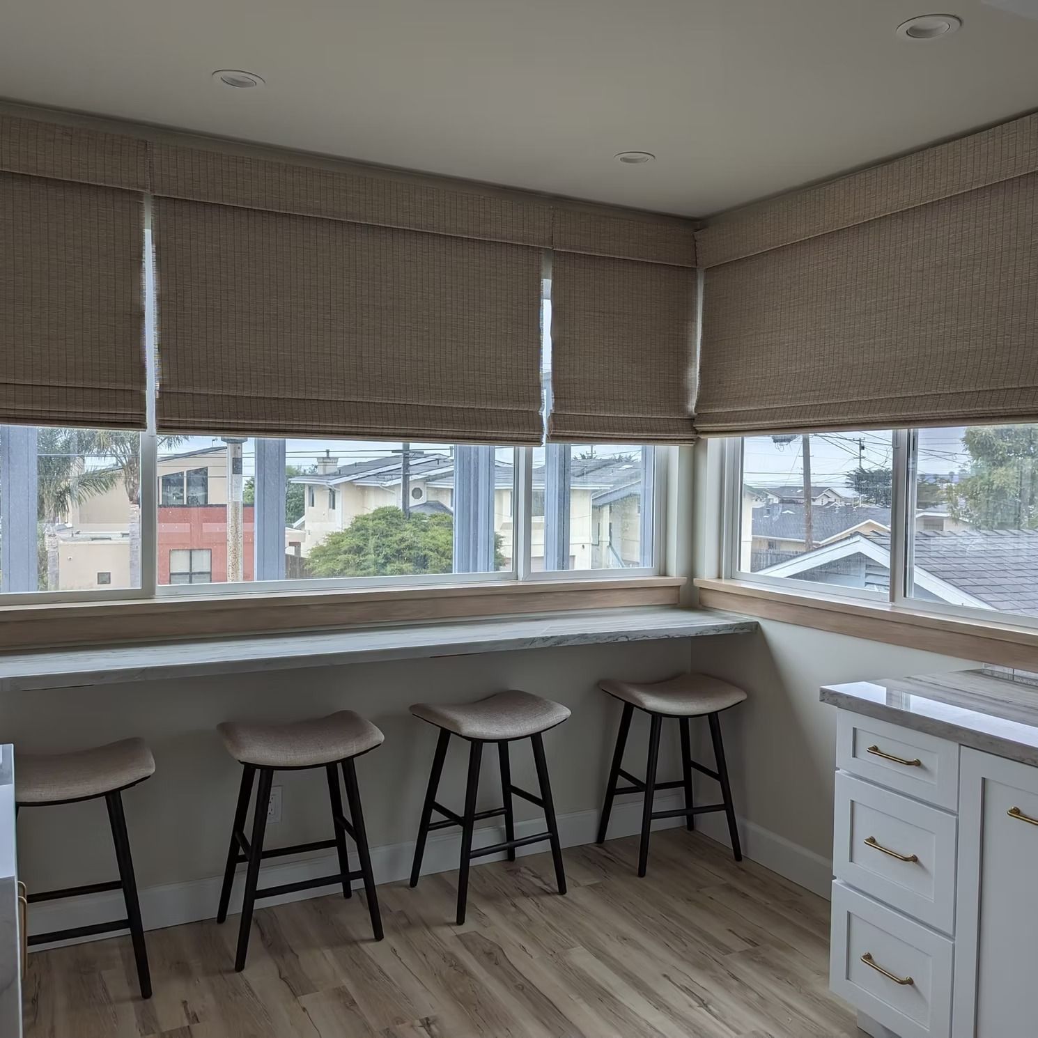 Window seat with four stools under large woven blinds in a bright kitchen nook