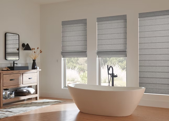 Modern bathroom with a freestanding tub, wood vanity, and three windows with blinds.