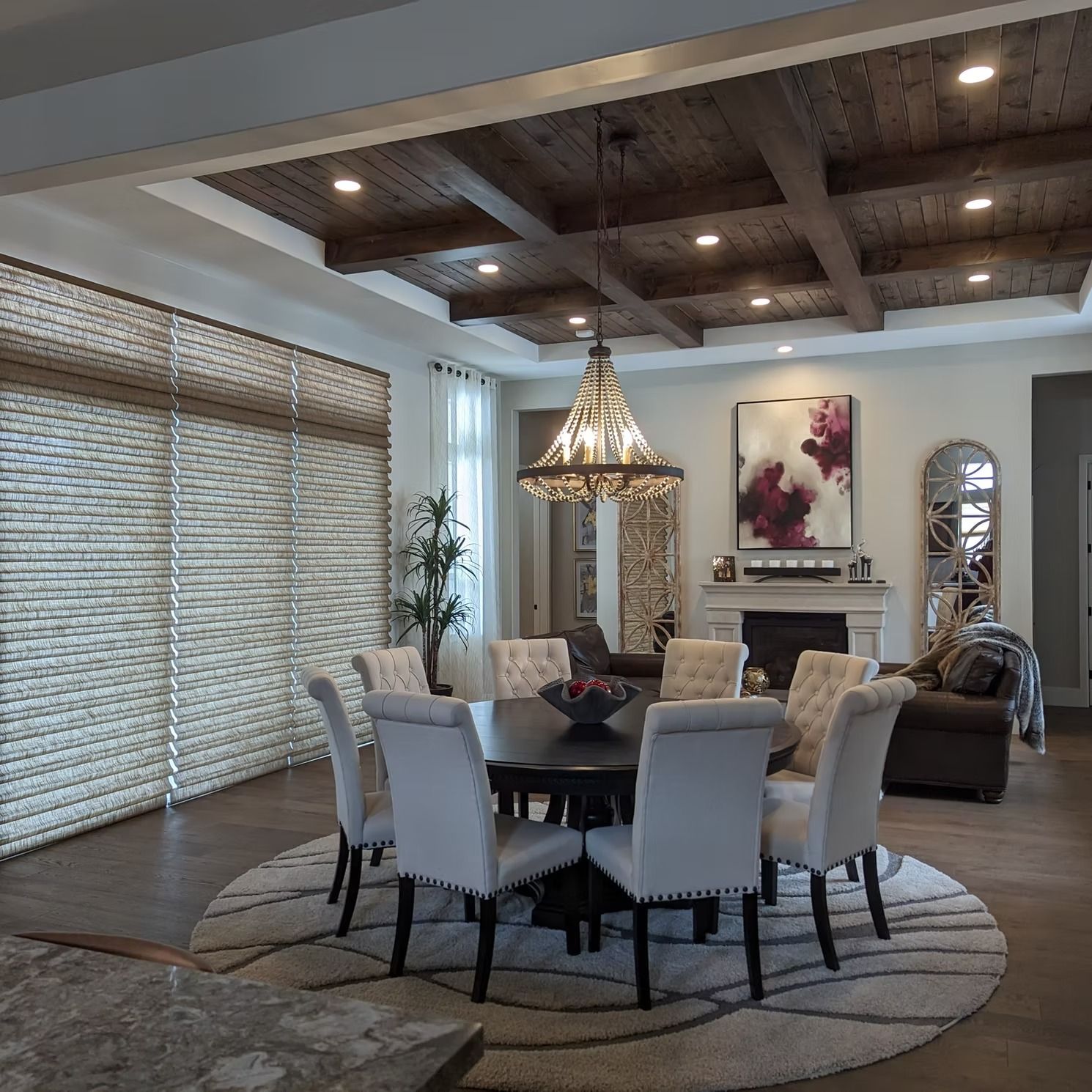 Elegant dining room with chandelier, round table, upholstered chairs, and large window blinds