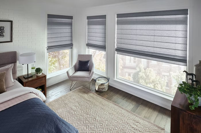 Bright bedroom with gray blinds, large windows, bed, chair, and patterned rug