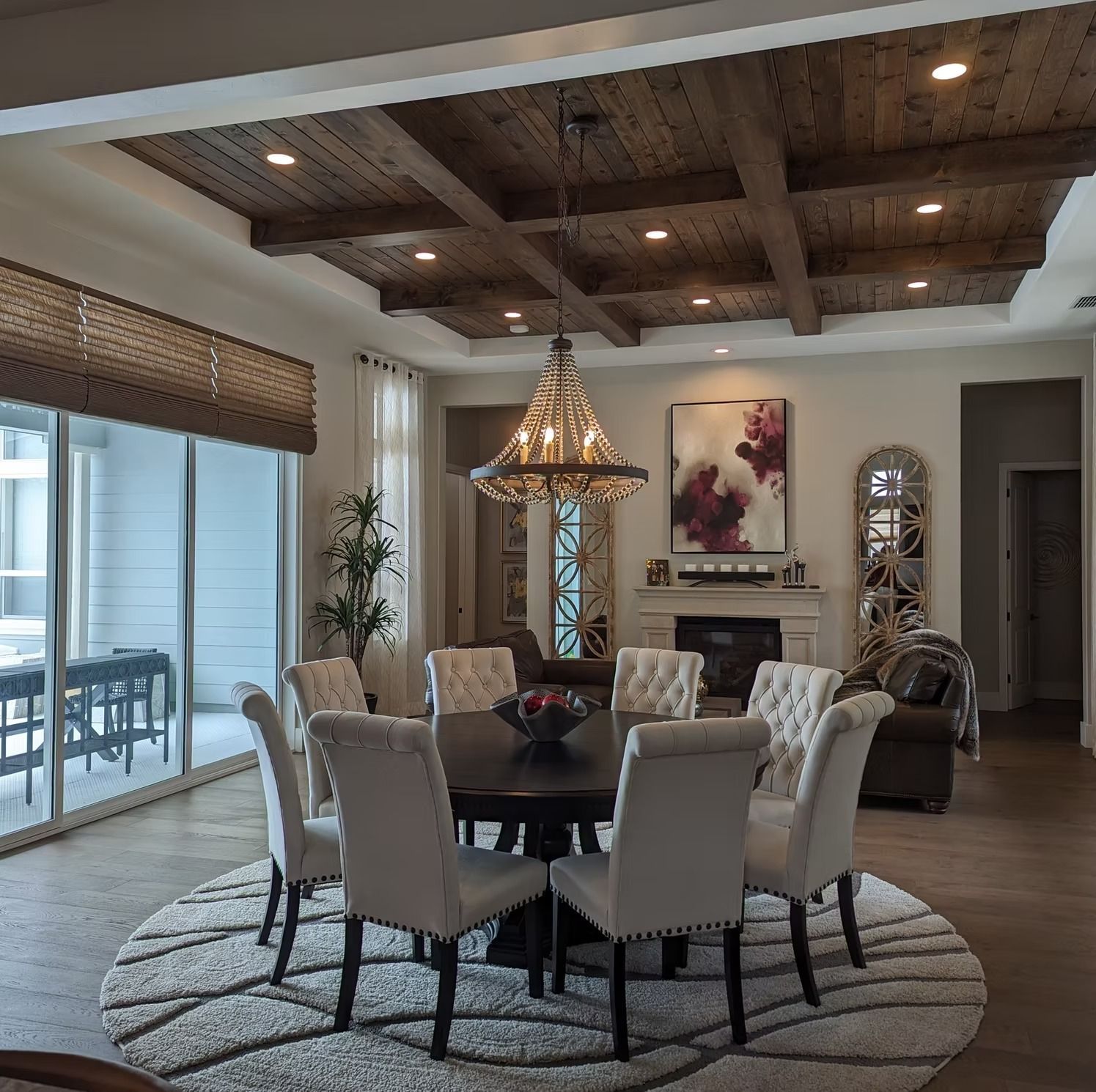 Elegant dining room with a round table, upholstered chairs, chandelier, and exposed wood-beam ceiling