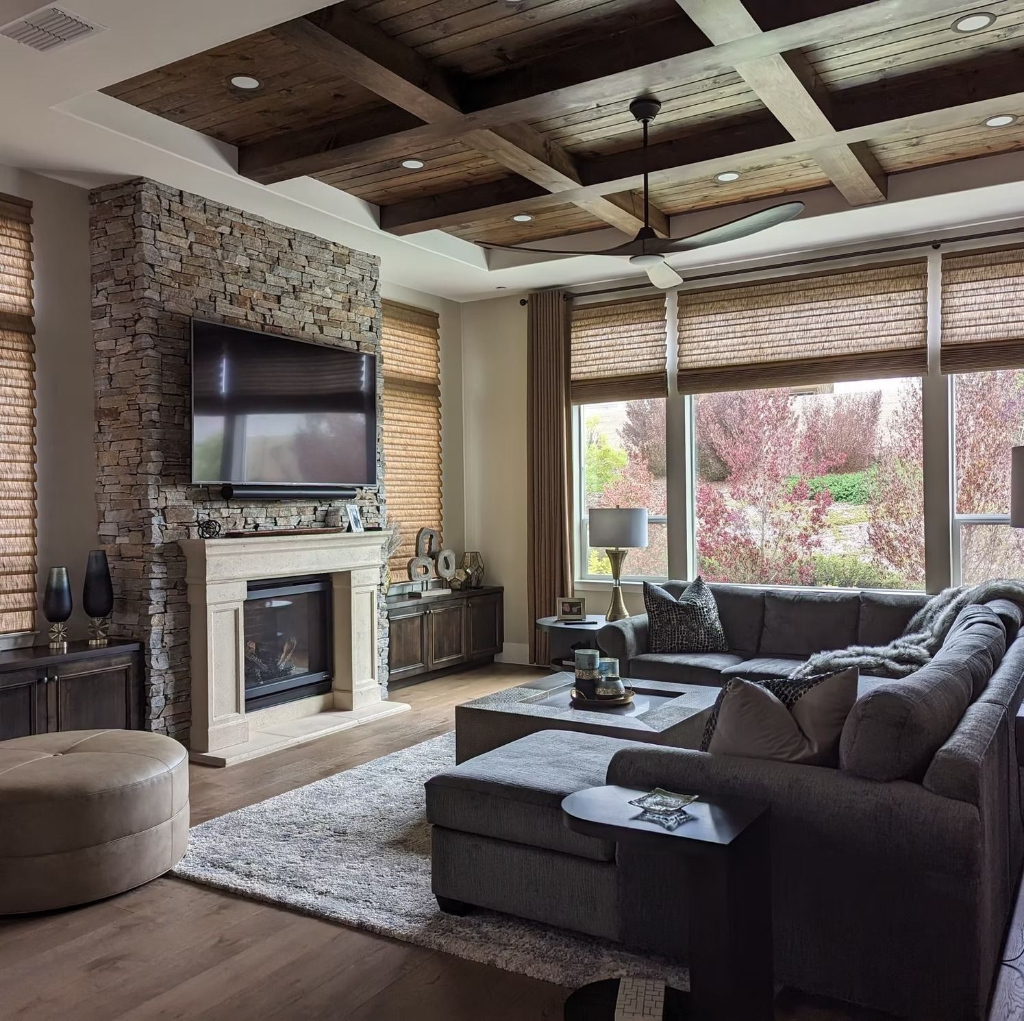 Modern living room with stone fireplace, wall-mounted TV, large sectional sofa, and wide windows.