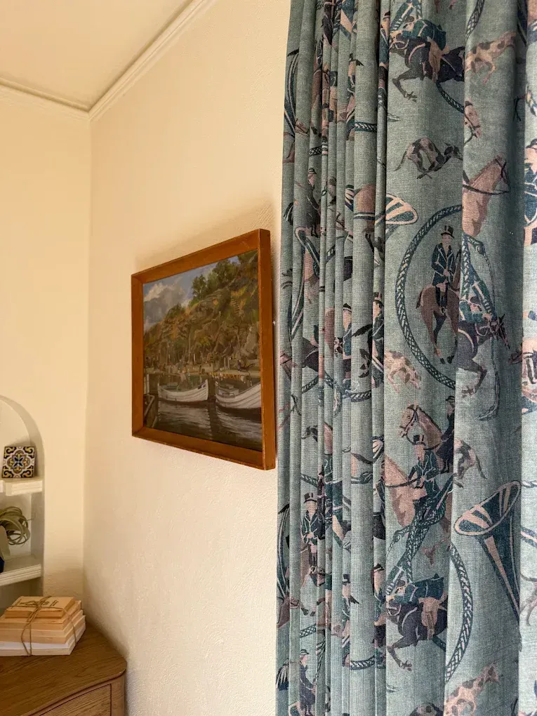 Curtained corner of a room with a framed landscape painting and a shelf with folded towels