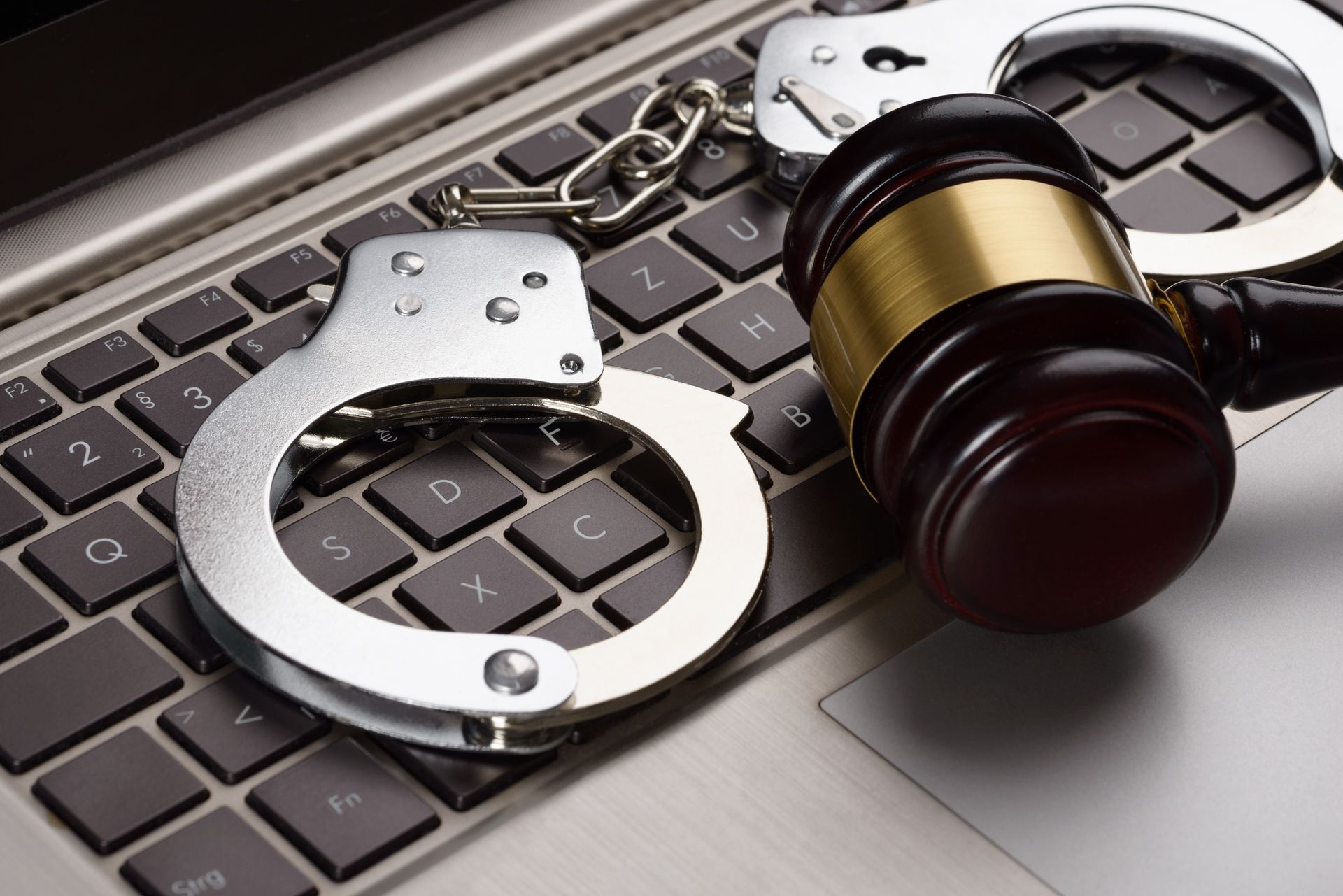 Handcuffs and a judge 's gavel are on a laptop keyboard.