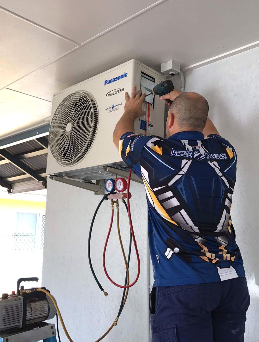 A Technician in Gray Workwear Installs or Services a Wall-Mounted Air Condition — Active Airconz in Winnellie, NT