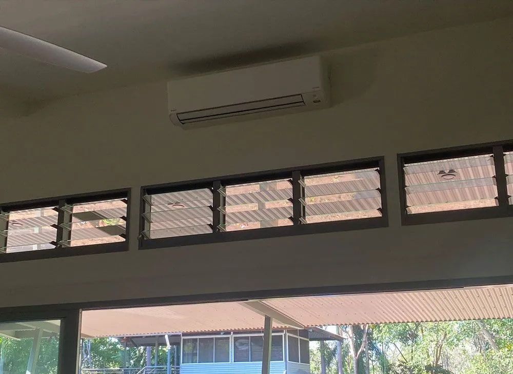 An Air Conditioning Unit Above a Row of Glass Louvre Windows — Active Airconz in Karumba, QLD