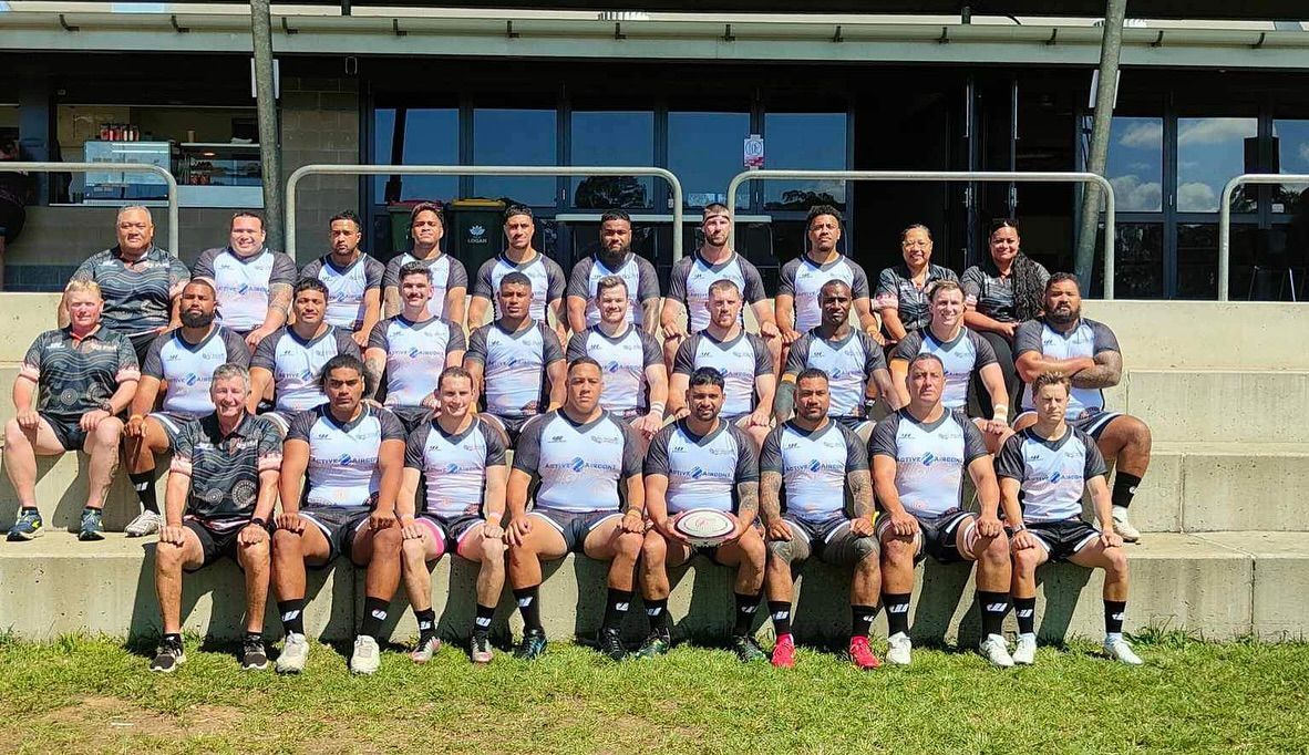Large group posing for a team photo outdoors in matching light blue uniforms in front of a building