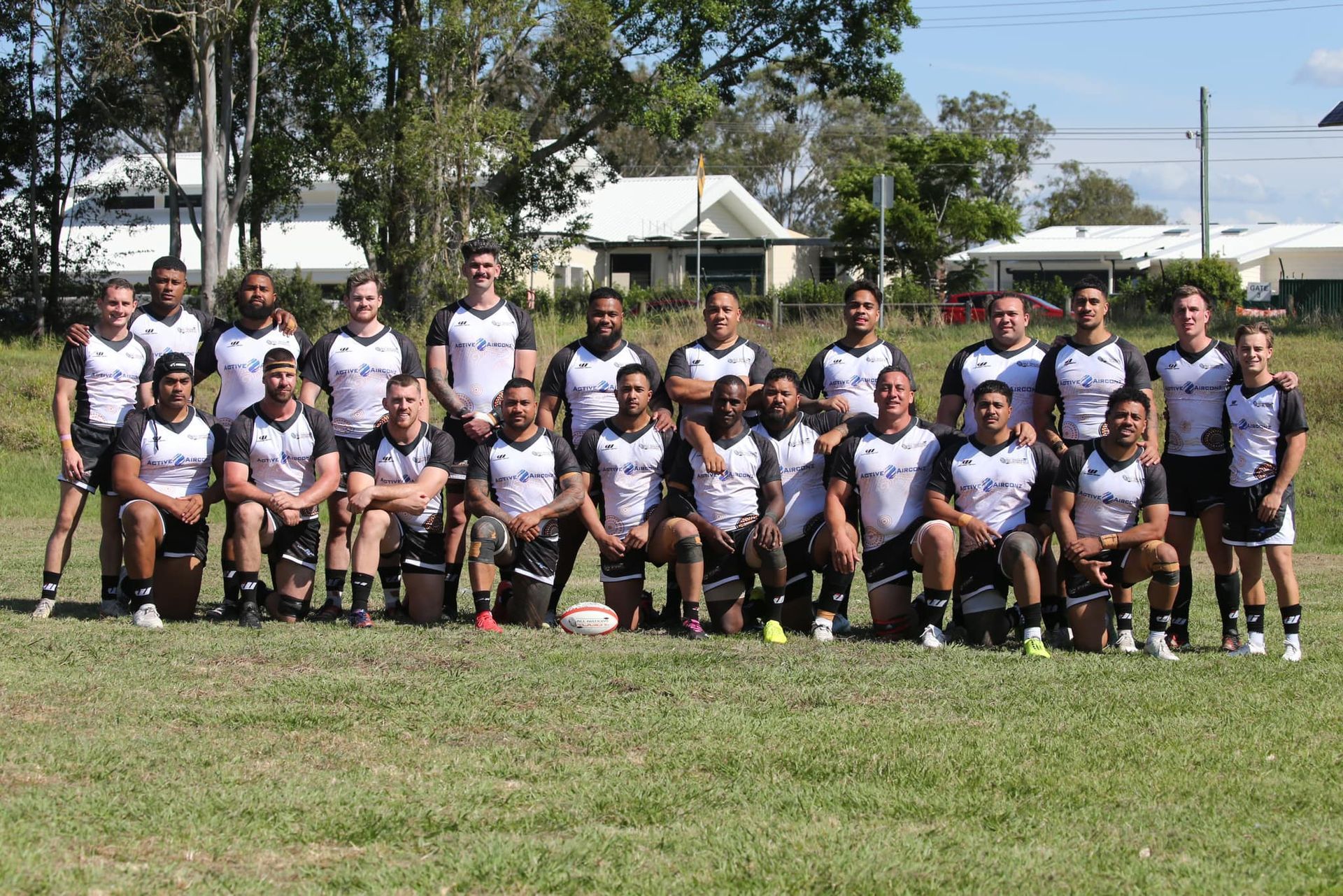 Large group of teammates posing outdoors on a grassy field, wearing matching black and white uniforms.