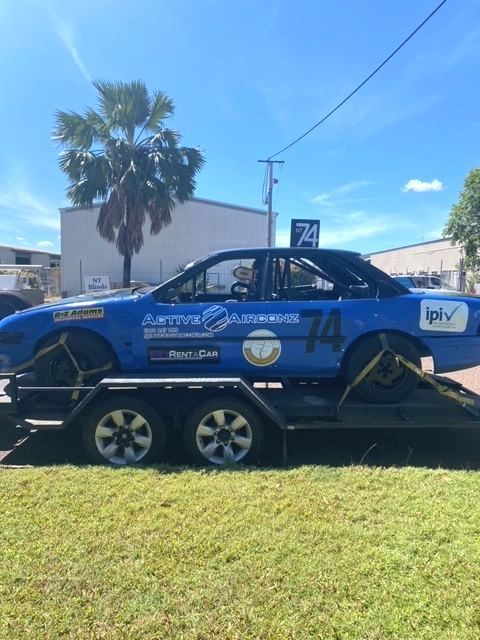 Blue Race Car on a Trailer in a Sunny Grassy Lot — Active Airconz in Winnellie, NT