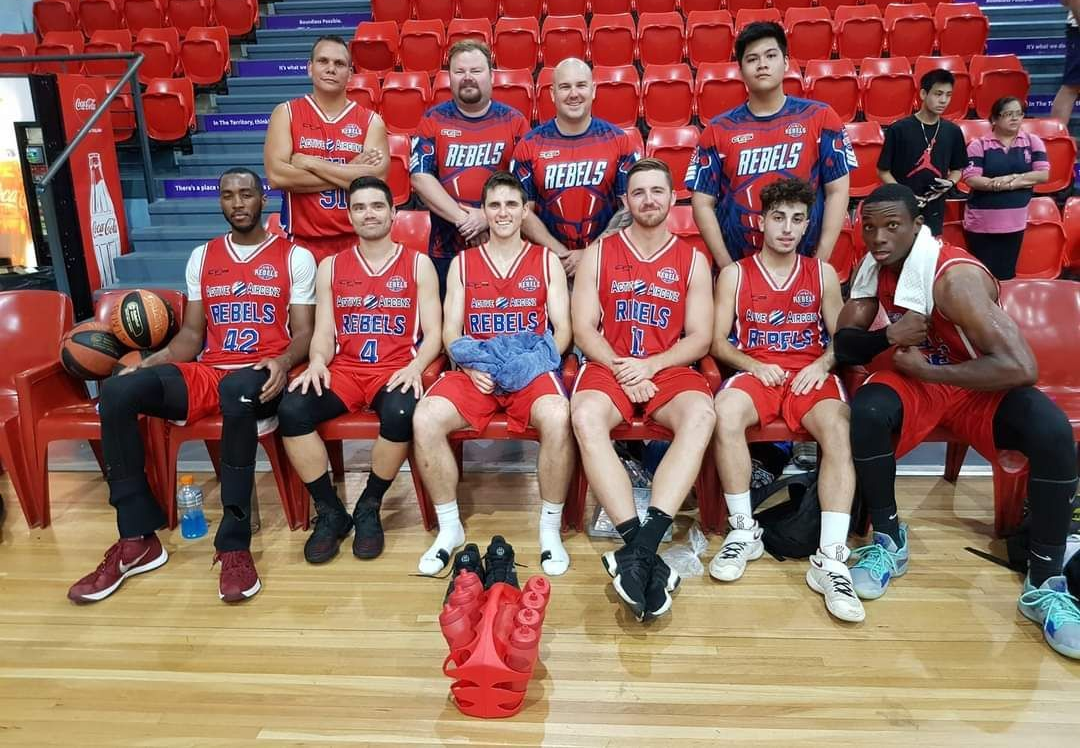 Basketball team posing in red uniforms on a court in front of red bleachers