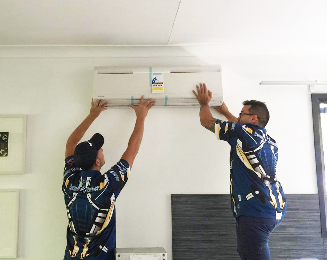 Two people installing an air conditioning unit on a white wall indoors. — Active Airconz in Gold Coast, QLD