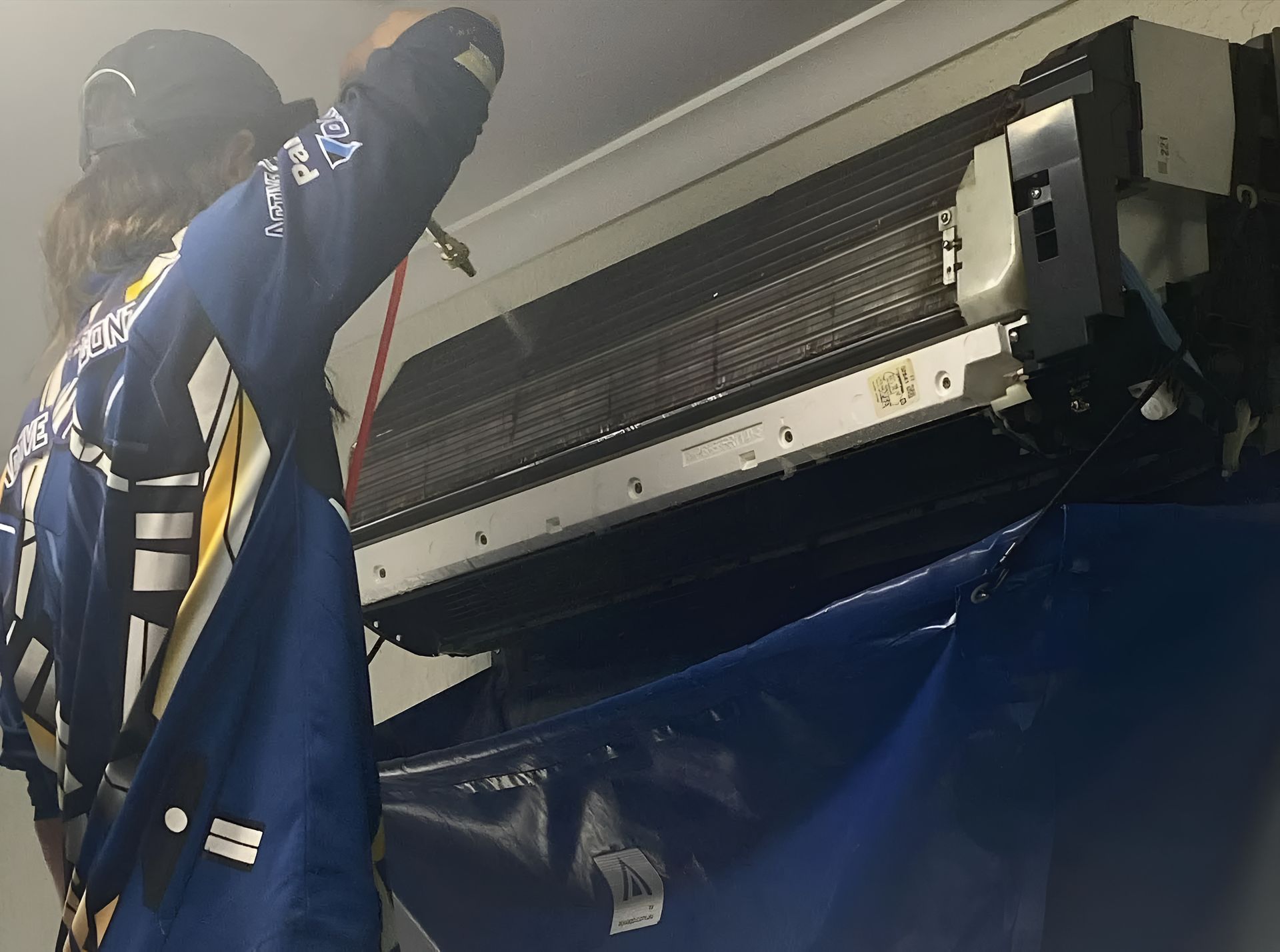 Technician in blue uniform cleaning a wall-mounted air conditioner unit. — Active Airconz in Rockhampton, QLD