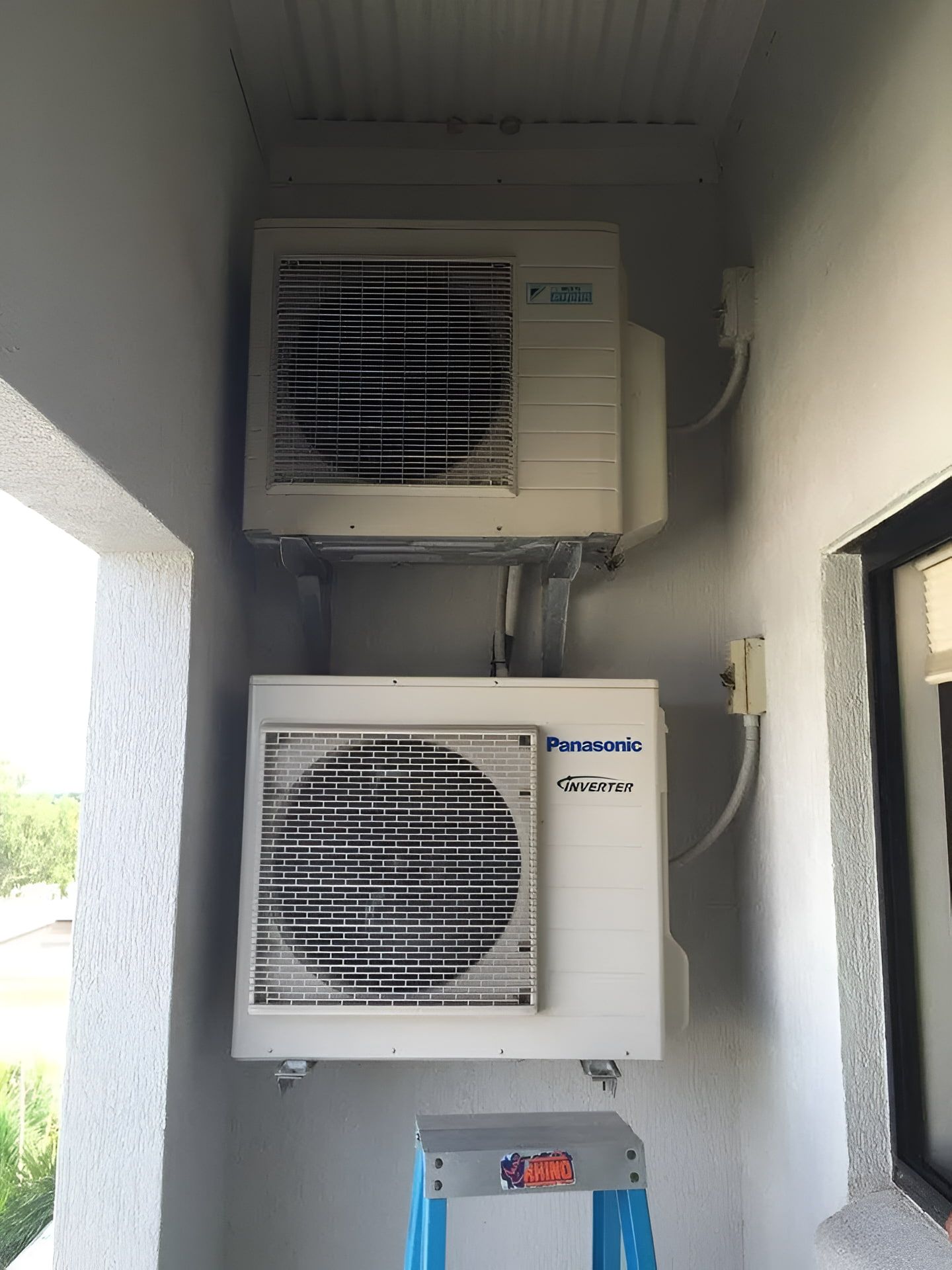 Two white air conditioning units mounted on a gray wall in a corner, with a ladder below. — Active Airconz in Toowoomba, QLD