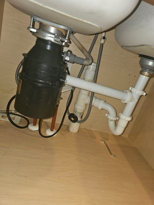 Under-sink plumbing with white pipes and a black garbage disposal unit under a sink.