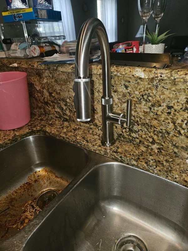 Kitchen sink with chrome faucet, granite countertop, and a pink cup in the background.