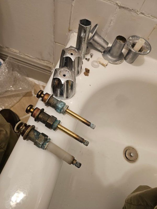 Bathroom sink with a detached faucet fixture and four valve cartridges laid out on the counter.