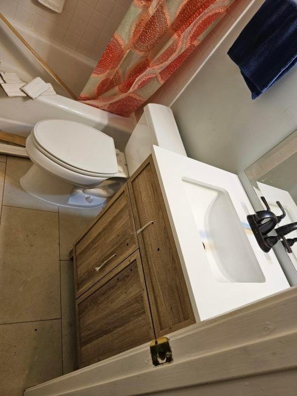 Small bathroom with toilet, wood vanity, white sink, and orange shower curtain