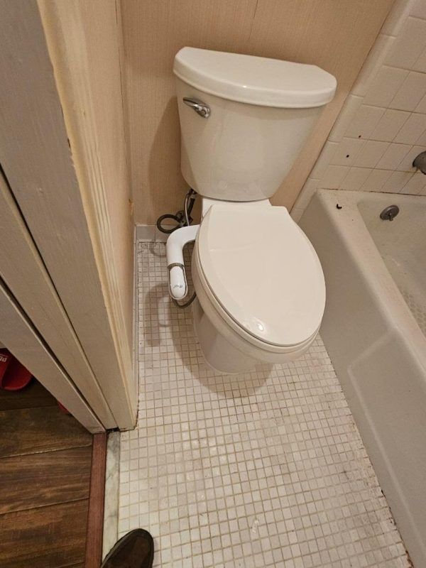 Compact bathroom with a white toilet beside a bathtub and tiled floor.