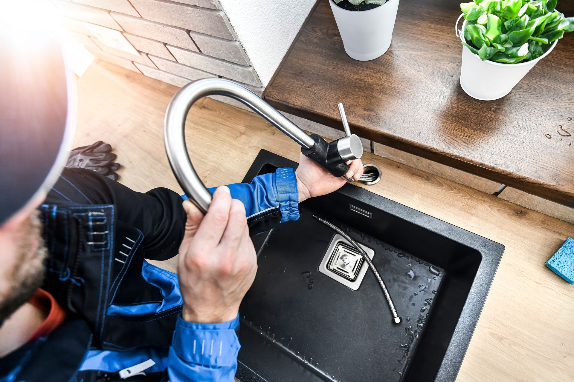 Plumber installing a faucet over a kitchen sink, with tools and a blue shirt visible.