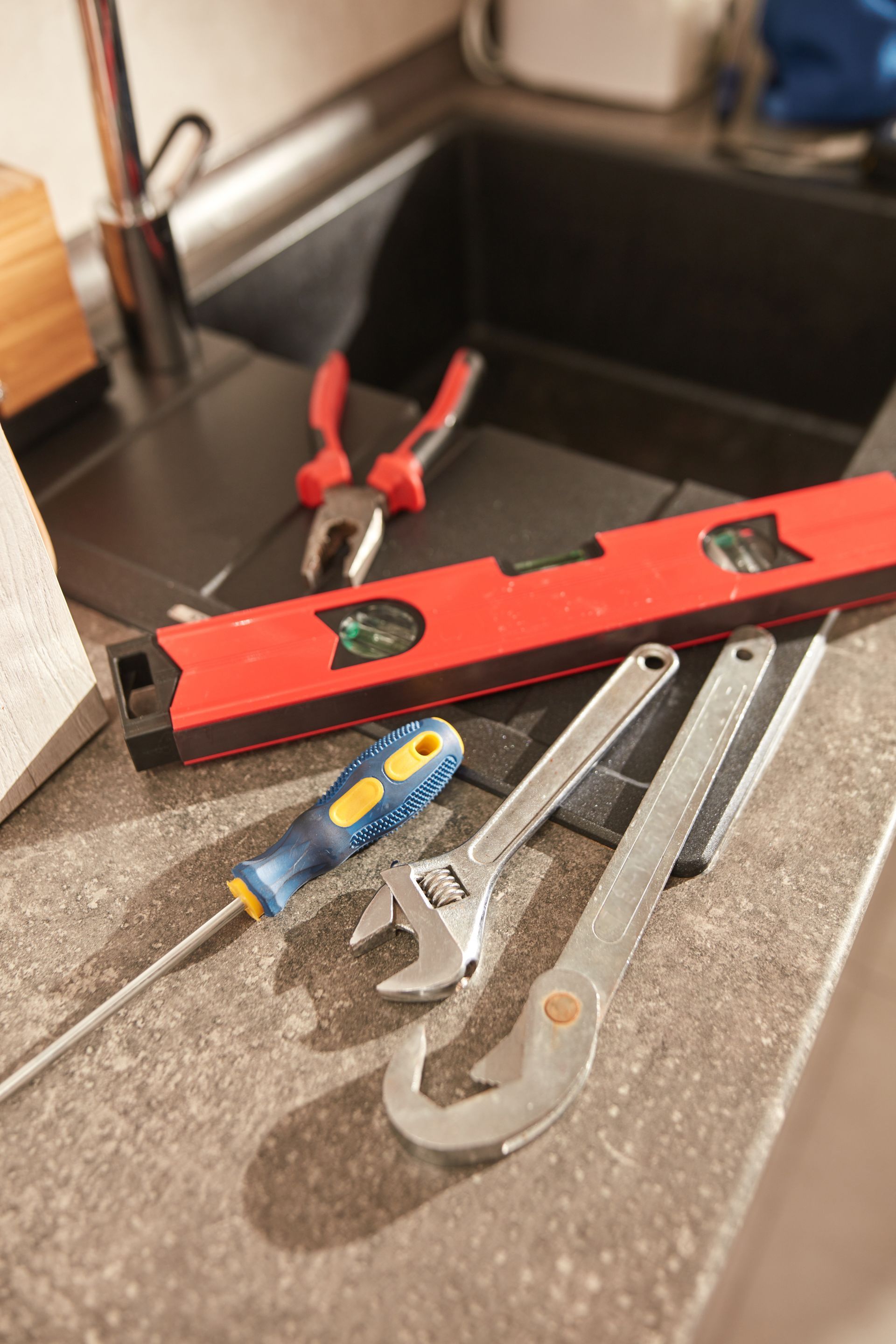 Hand tools on a kitchen counter, including a red level, pliers, screwdriver, and wrenches.