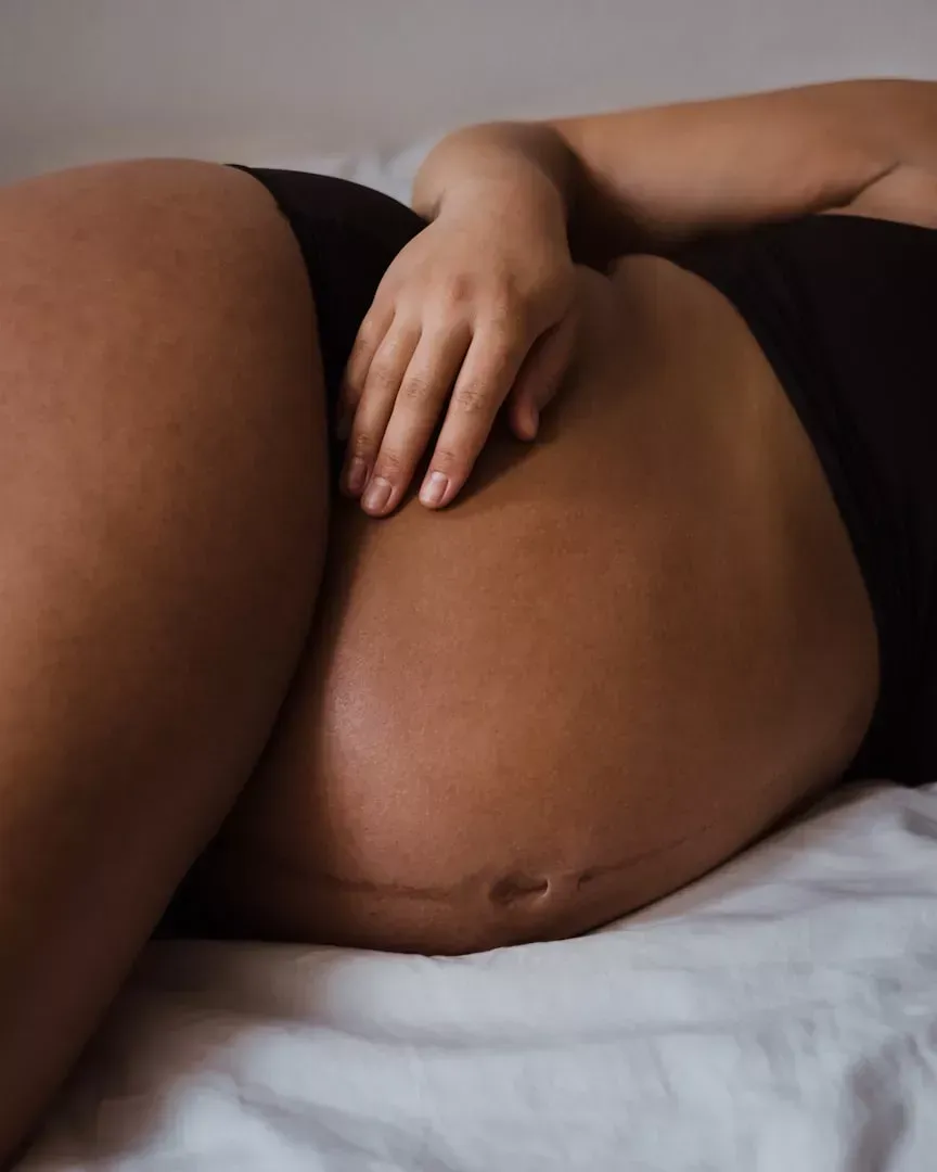 Pregnant belly resting on a bed, with a hand placed gently on top.