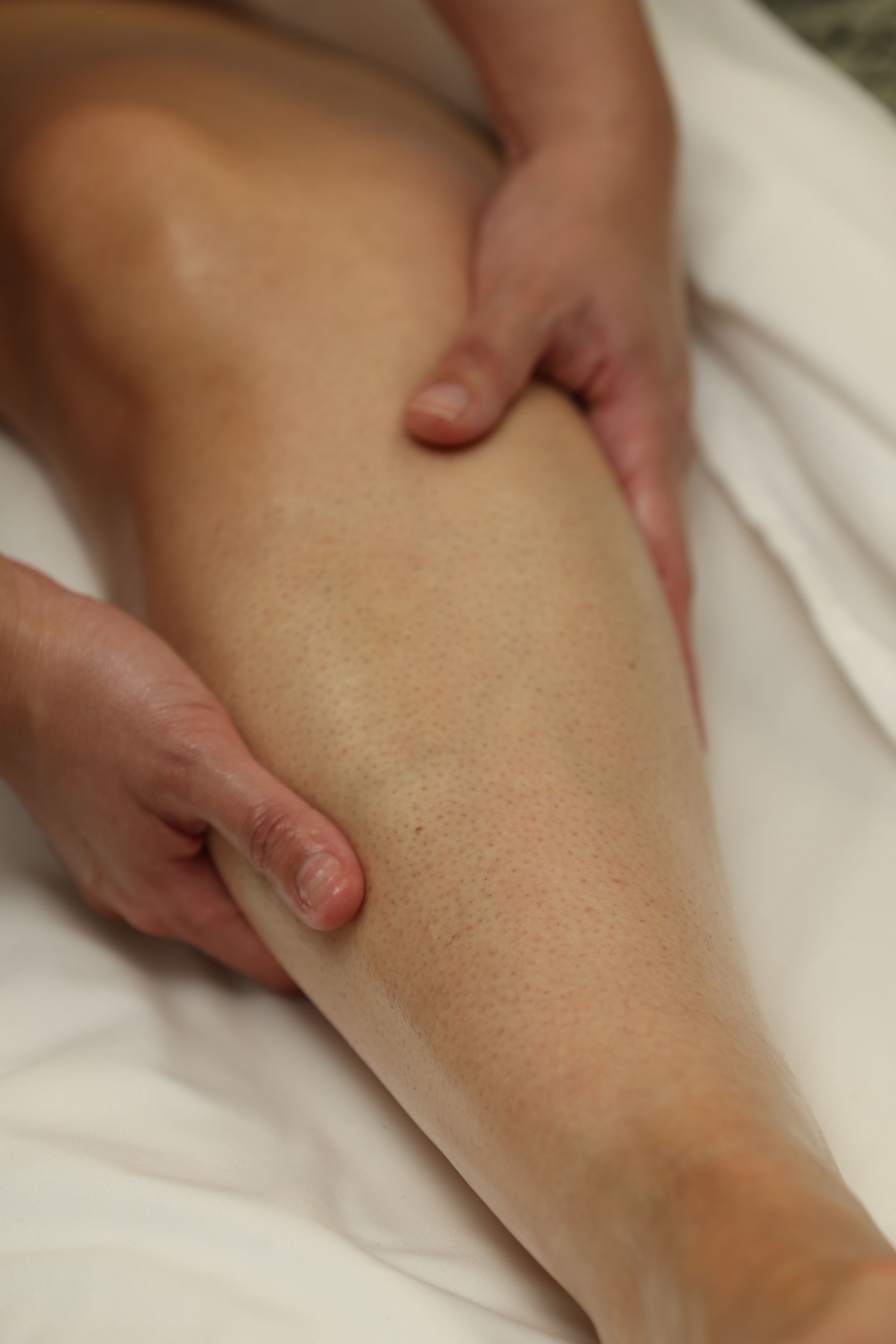 Hands massaging a person's lower leg on a white towel.